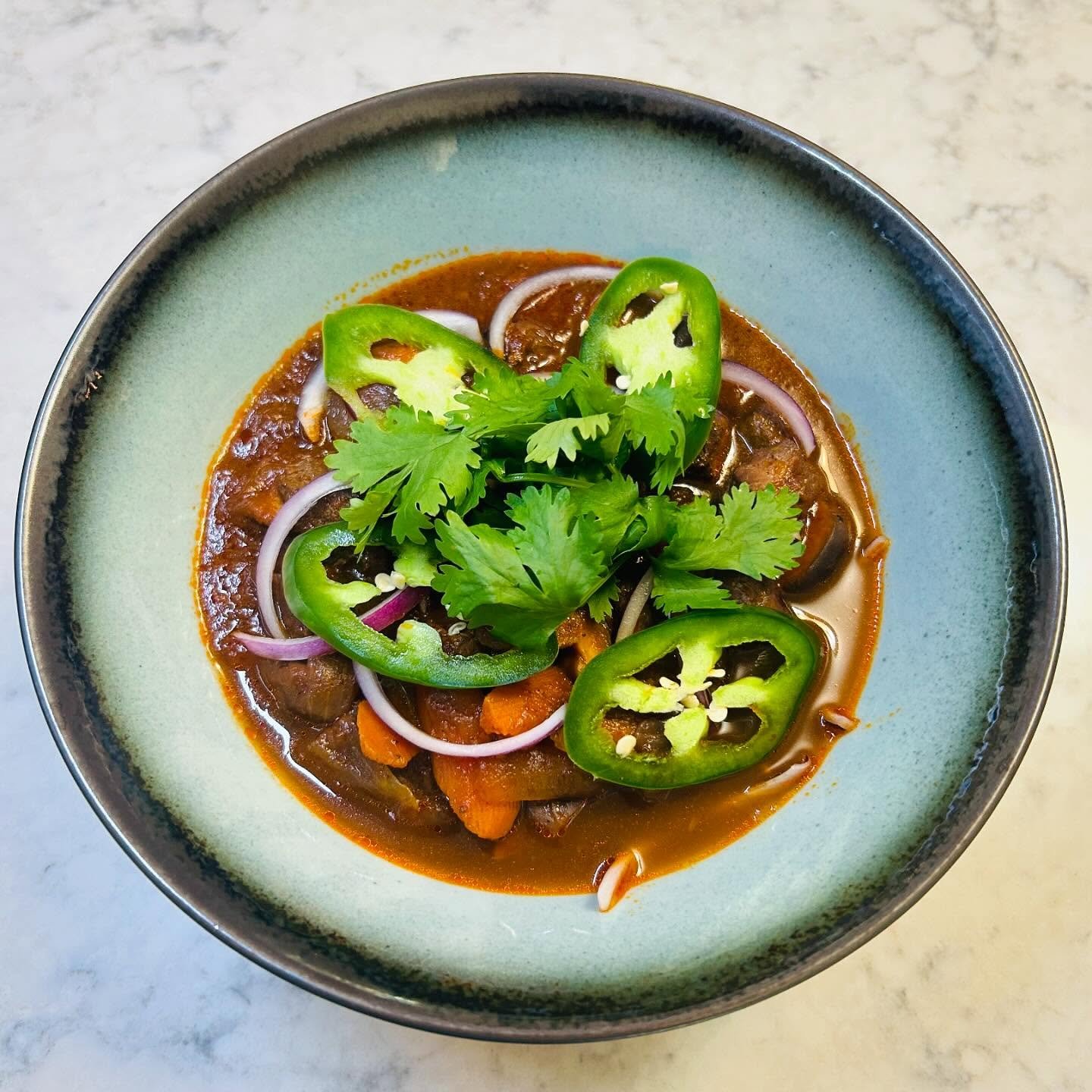 Bowl of beef stew with sliced jalapeños, red onions, and cilantro on top