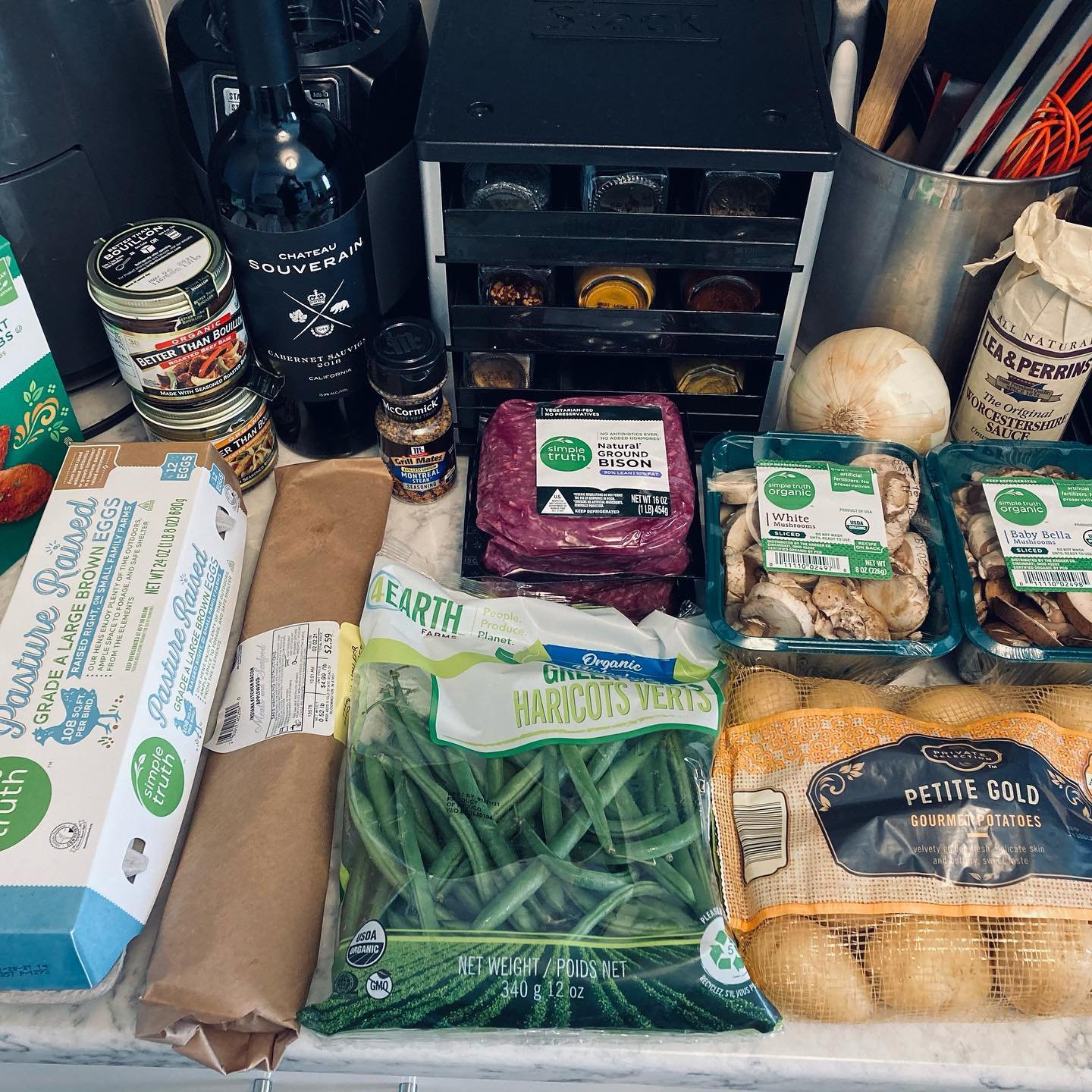 Grocery items including eggs, green beans, potatoes, mushrooms, ground beef, onion, assorted spices, wine, and various packaged foods on a kitchen counter.
