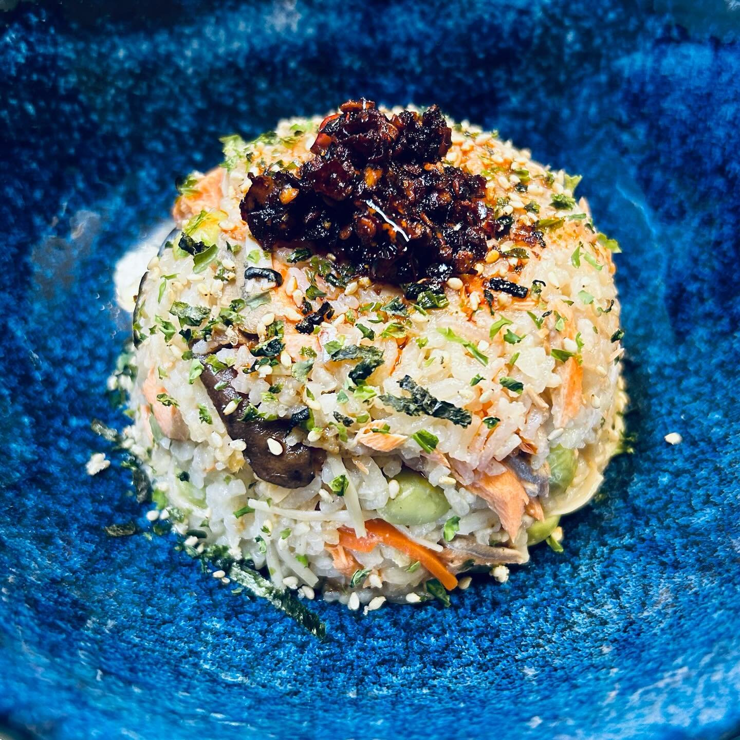A serving of rice mixed with vegetables, topped with a dark sauce and sprinkled with chopped herbs, served in a blue bowl.