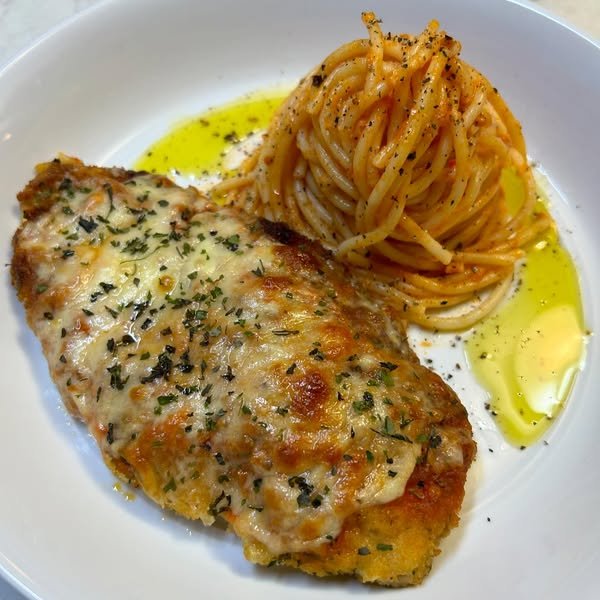 A plate with baked fish fillet topped with melted cheese and herbs, and a side of spaghetti pasta with tomato sauce, garnished with olive oil and black pepper.