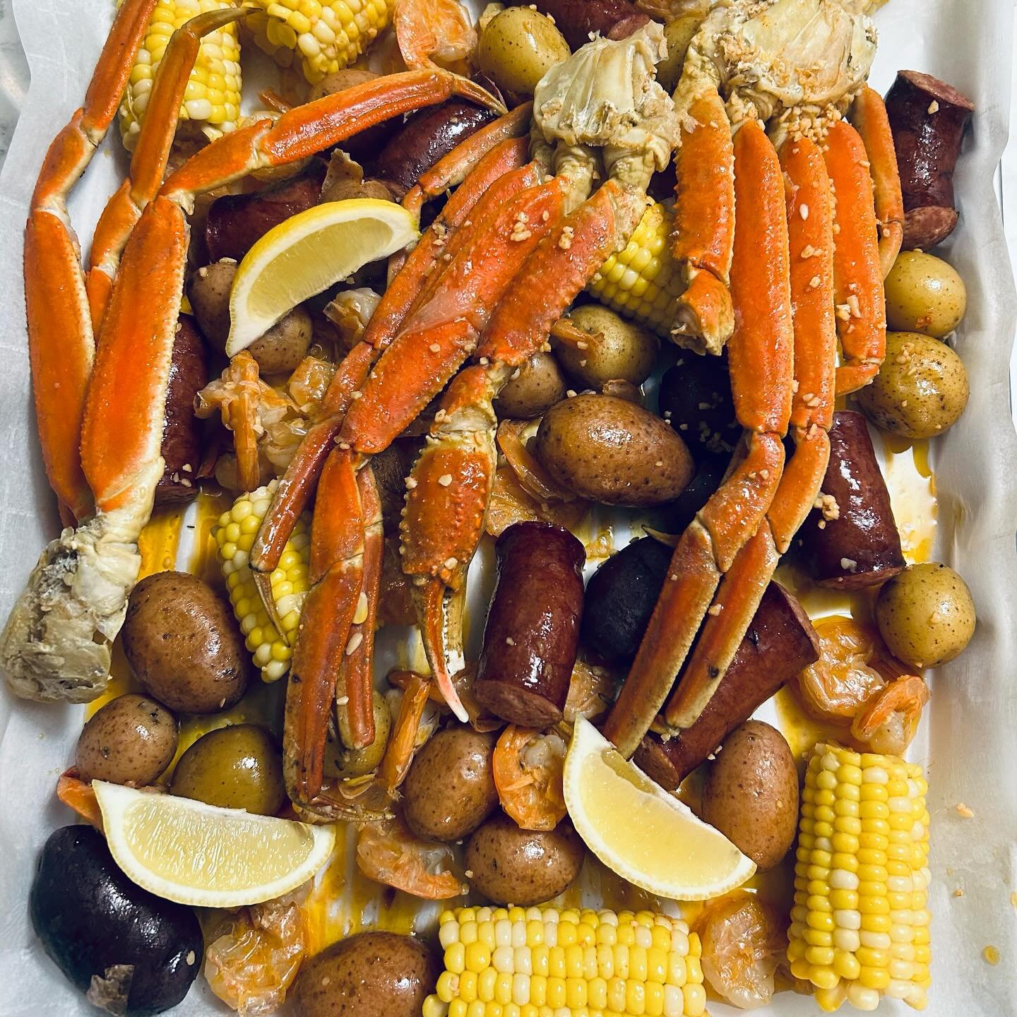 Seafood boil with crab legs, shrimp, sausage, potatoes, corn on the cob, and lemon wedges