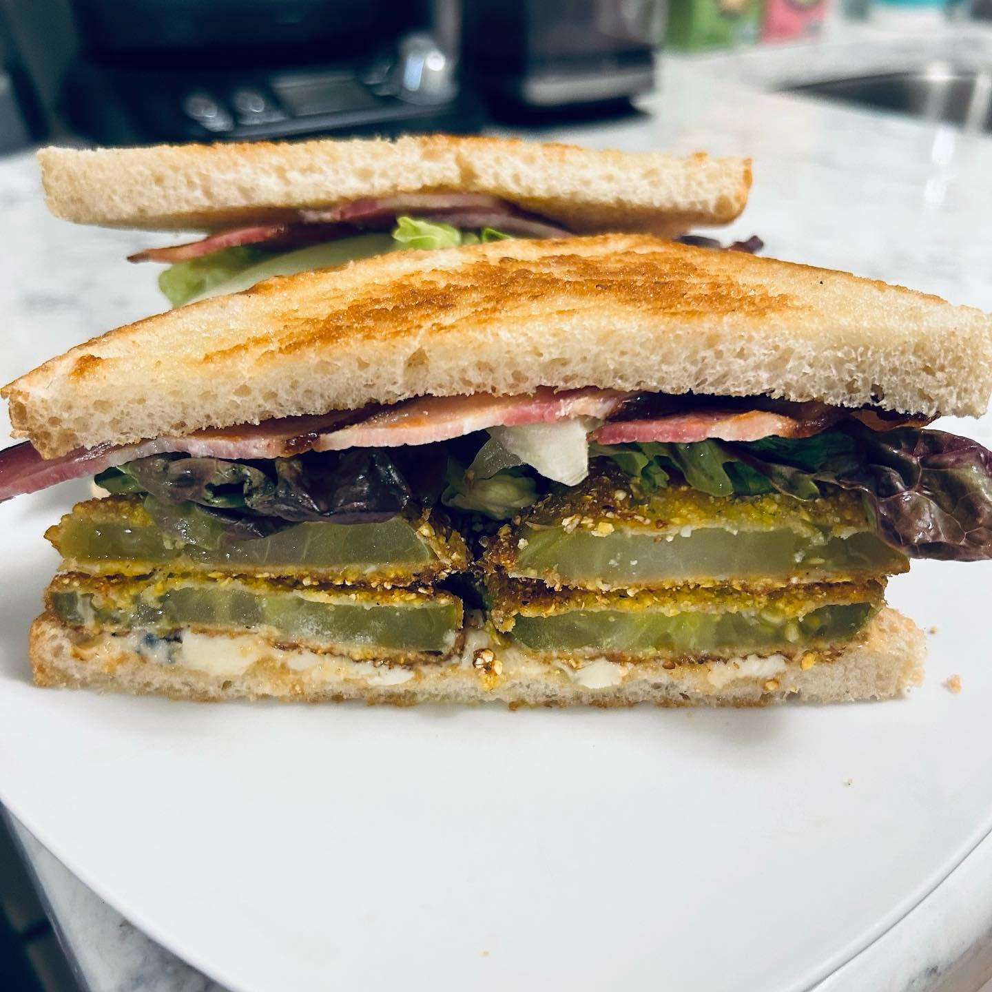 Cross-section of a sandwich with pickles, lettuce, cheese, ham, and bread on a white plate.