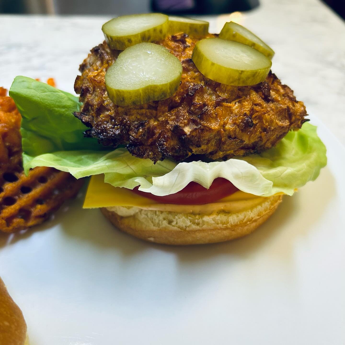 A burger with lettuce, tomato, cheese, a pickled bun, a large fried chicken patty topped with pickles, and a sandwich bun.
