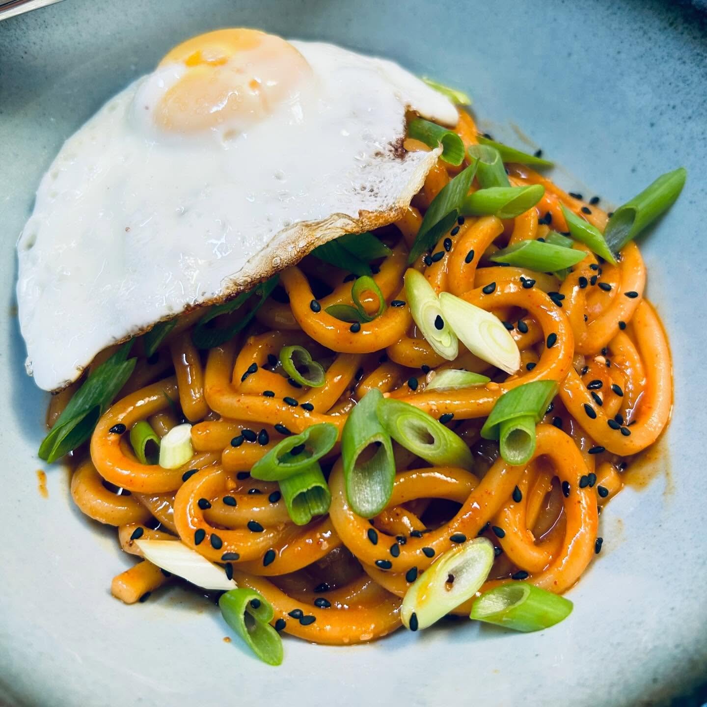 Cooked noodles with green onions, black sesame seeds, and a fried egg on top