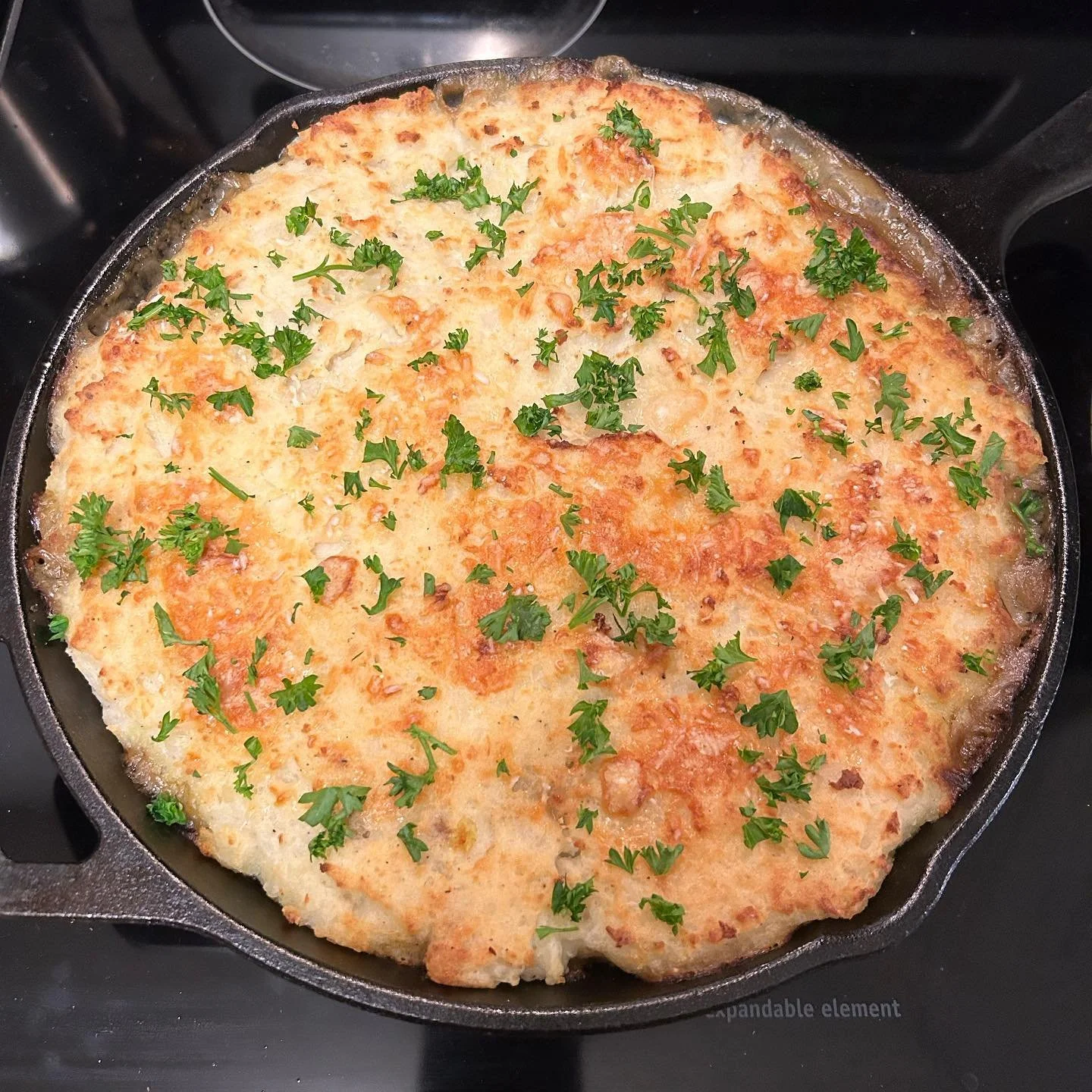 A skillet of baked cheesy bread topped with chopped parsley.