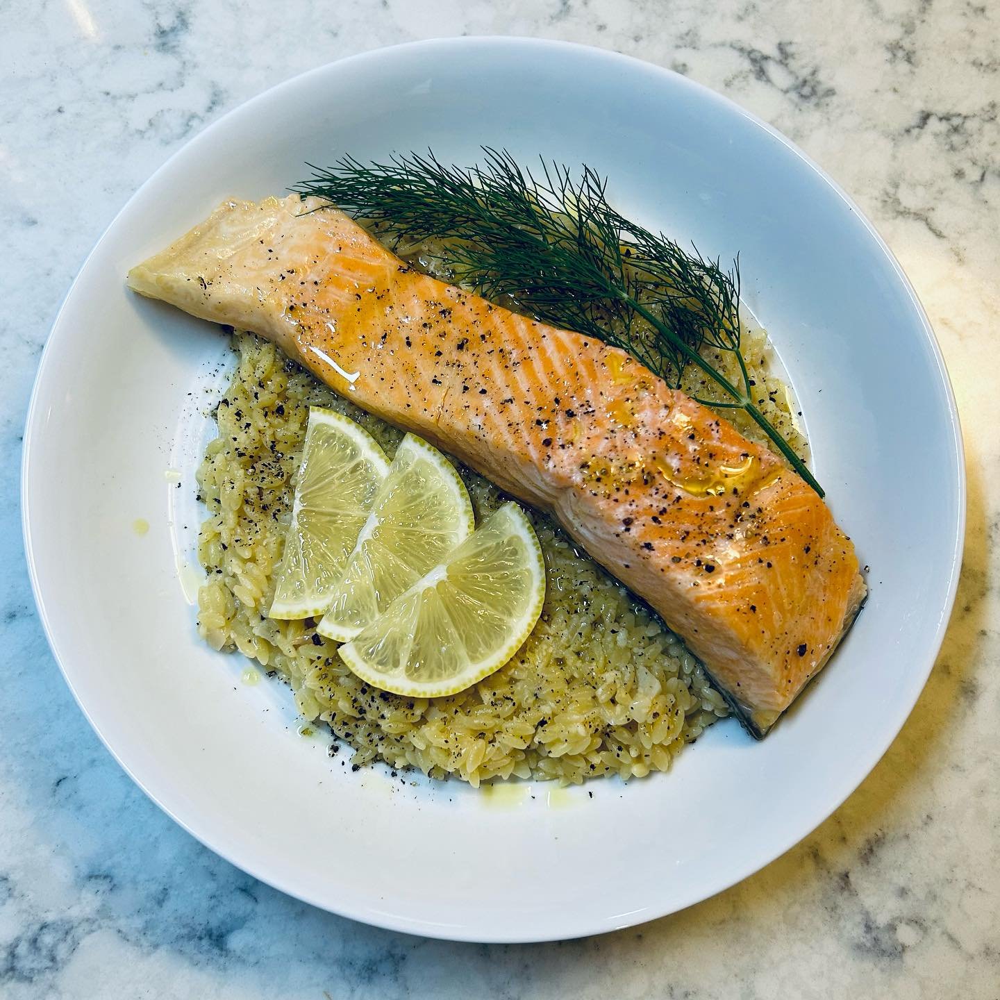 Baked salmon fillet with lemon wedges, dill garnish, served over rice on a white plate.