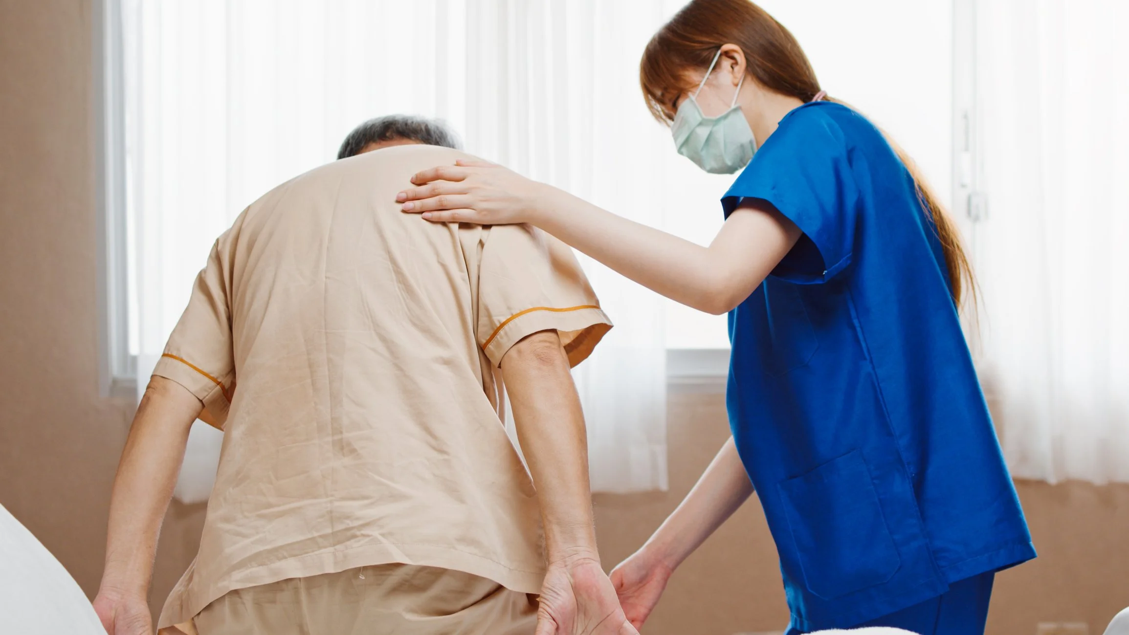 Une infirmière aide un patient à se lever ou à marcher, dans une pièce lumineuse.