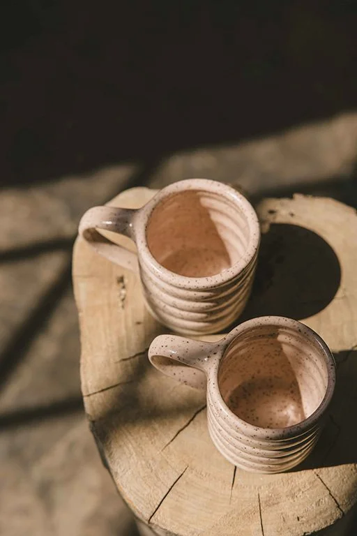 Two ceramic mugs with handles, placed on a wooden surface, viewed from above with sunlight casting shadows.