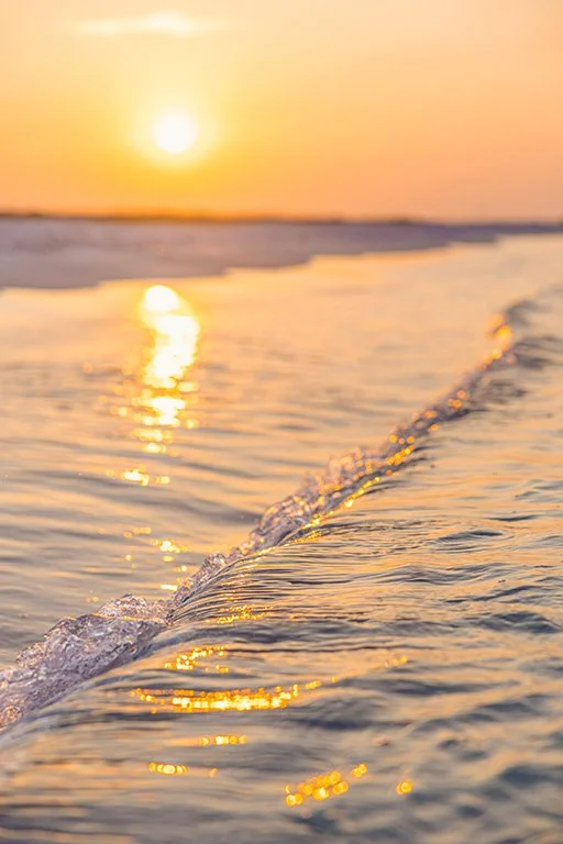 Sunset over the ocean with gentle waves reflecting the orange glow of the sky.