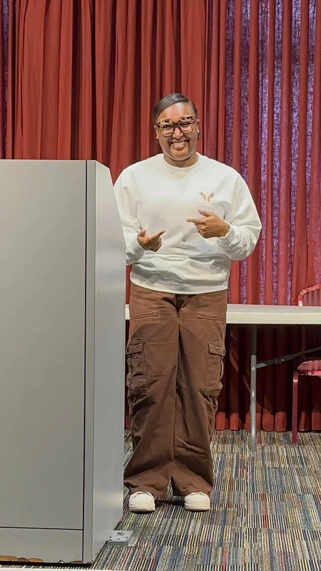 A woman wearing glasses and a white jacket speaking into a microphone during a discussion, with another woman in pink listening attentively.