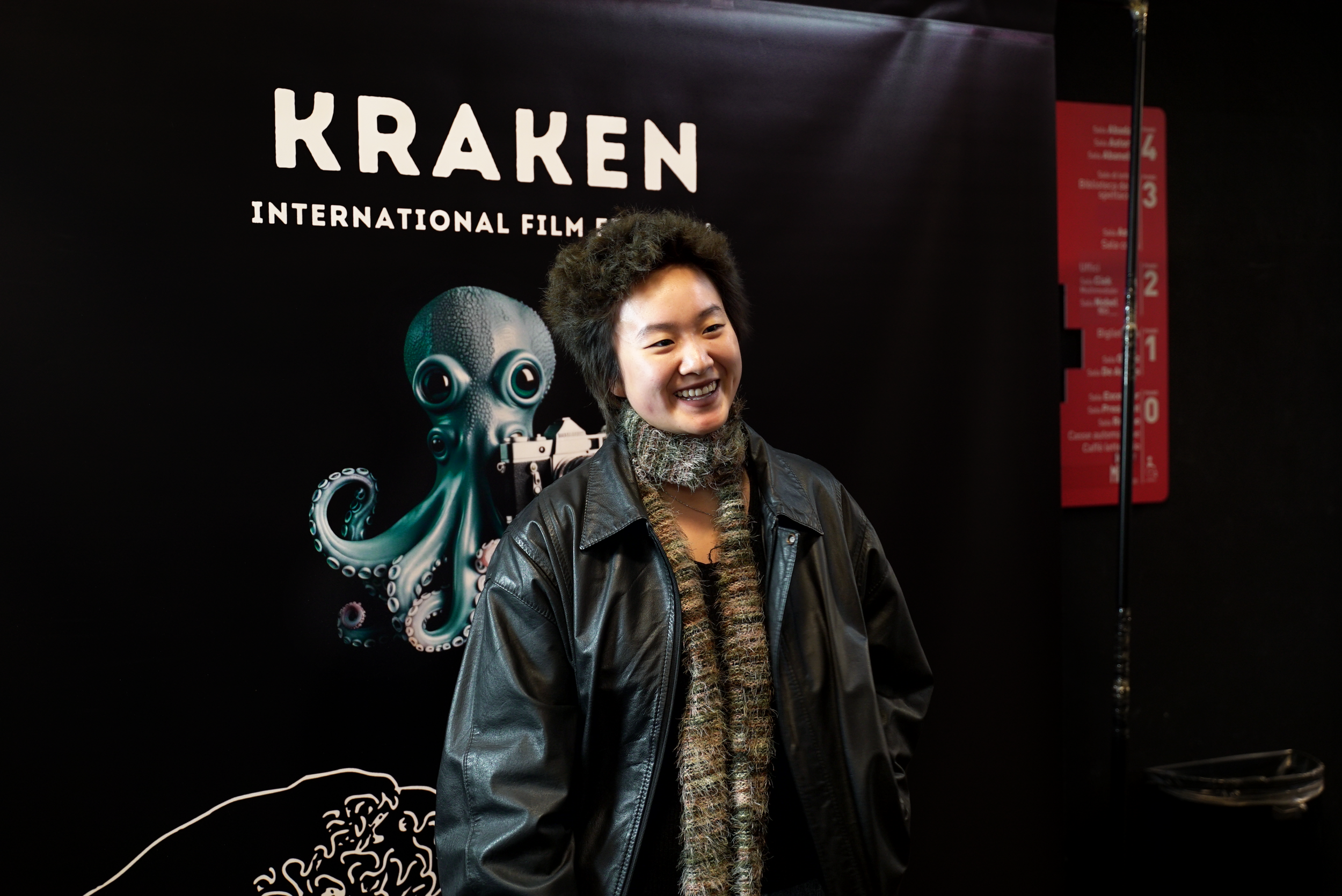 Person smiling in front of Kraken International Film Festival backdrop with octopus graphic.