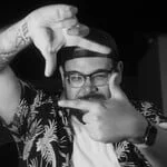 Person with glasses and cap making a framing gesture with hands