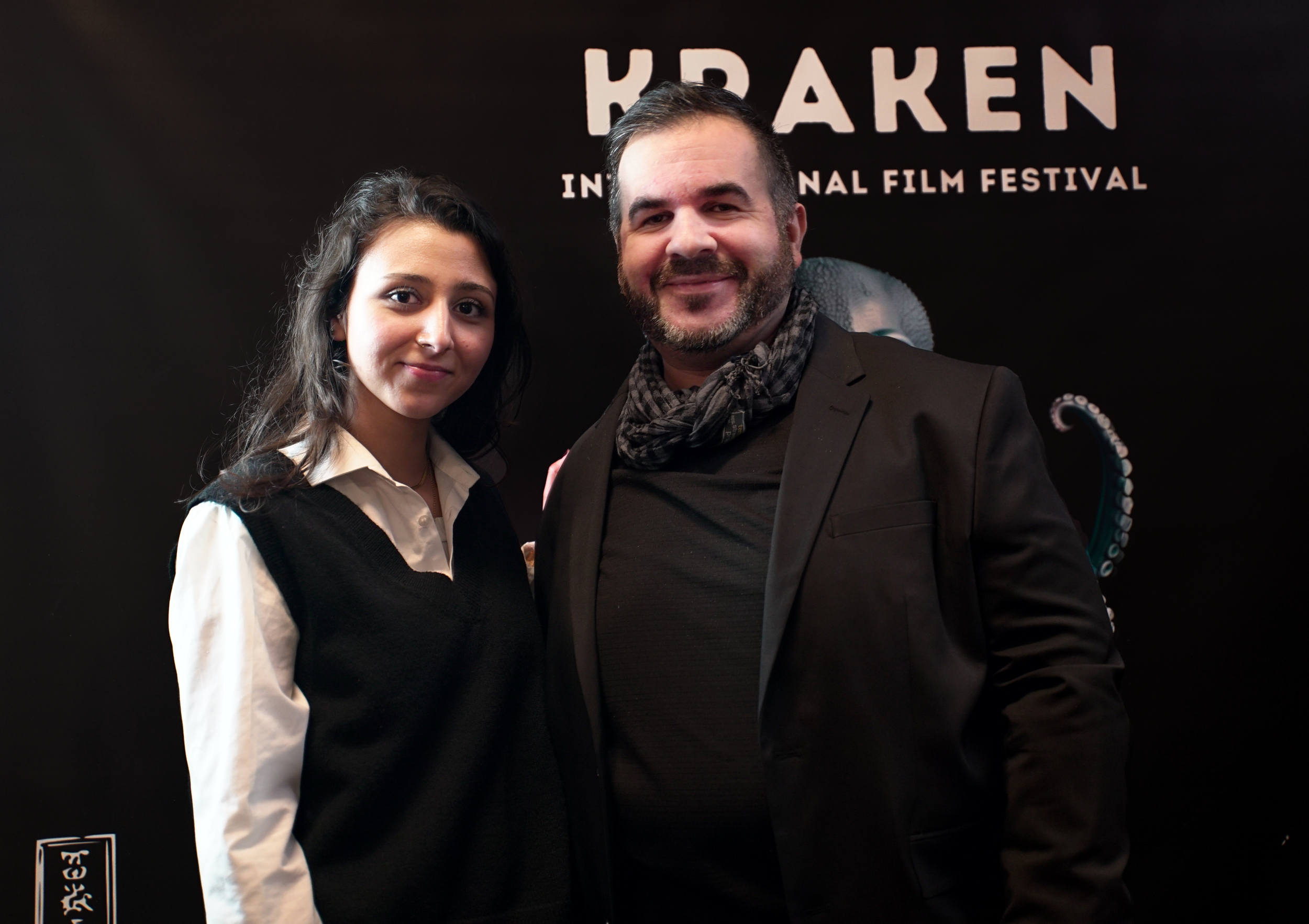 Two people posing in front of a "Kraken International Film Festival" backdrop.