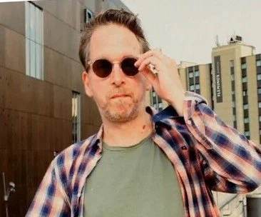 Man with sunglasses and plaid shirt outdoors in urban setting