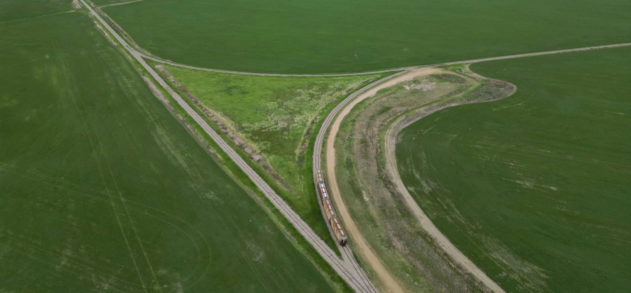 Aerial view of a train curving through lush green fields on a set of railway tracks.