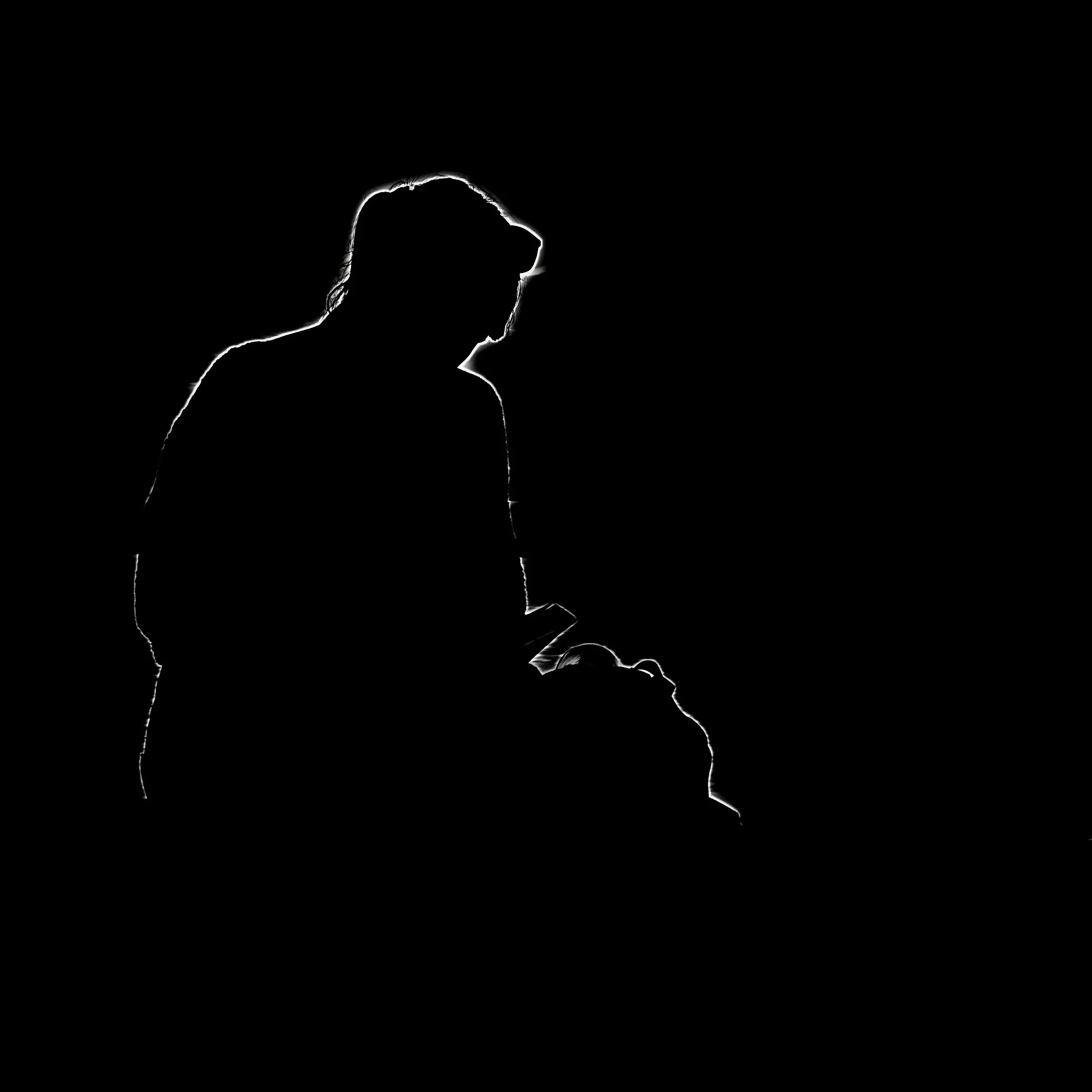 Schwarz-Weiß-Silhouette einer sitzenden Person, sichtbar von den Schultern aufwärts, mit Fokus auf den Kopf in Profilansicht gegen schwarzen Hintergrund.