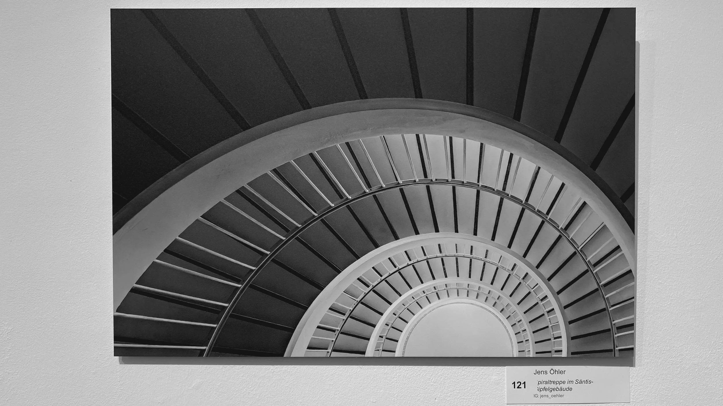 Schwarz-Weiß-Fotografie einer spiralförmigen Treppe, die nach oben führt, mit Stufen und Geländern in einem Gebäudeflug.
