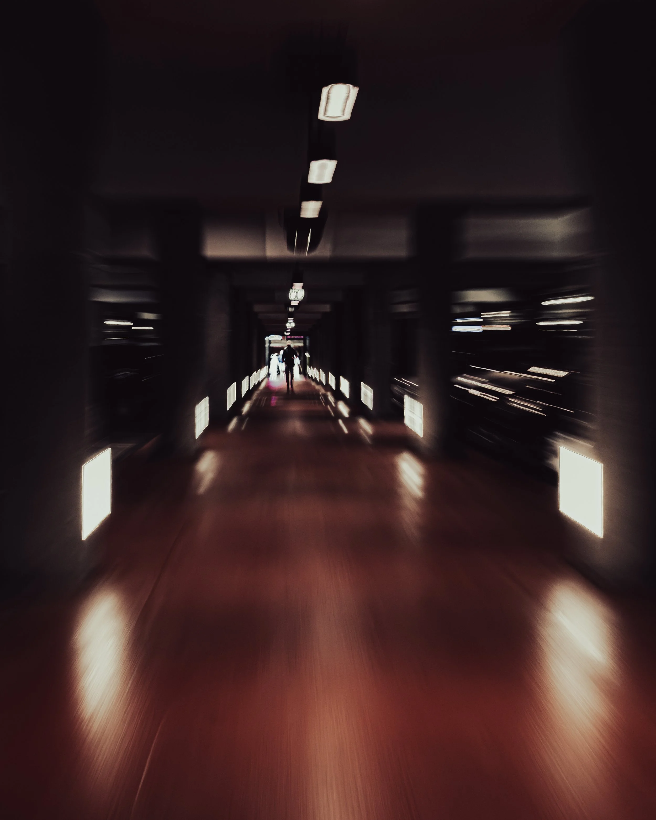 Ein dunkler Tunnel mit beleuchteten Seitenwänden und Personen, die durch ihn gehen, in einem unscharfen, bewegten Bild.