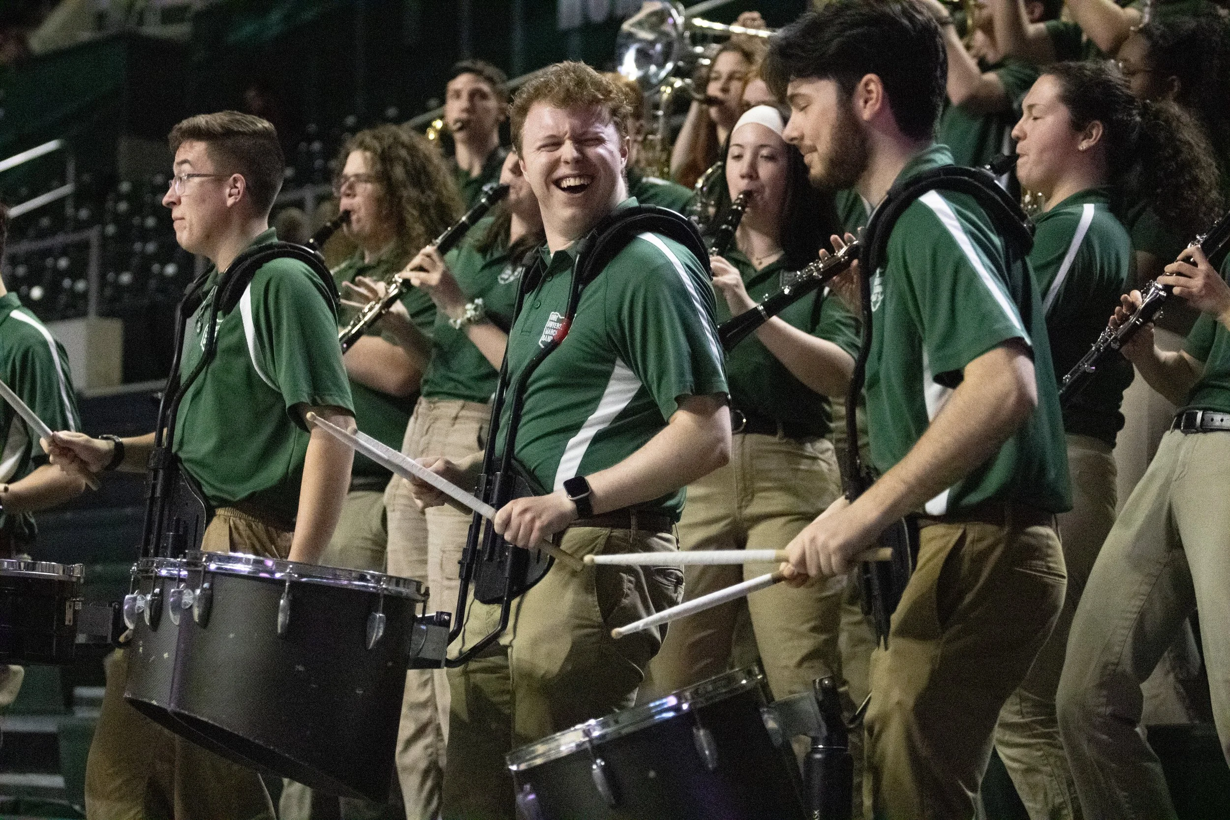 A group of young musicians in green shirts playing percussion and wind instruments at a band concert.