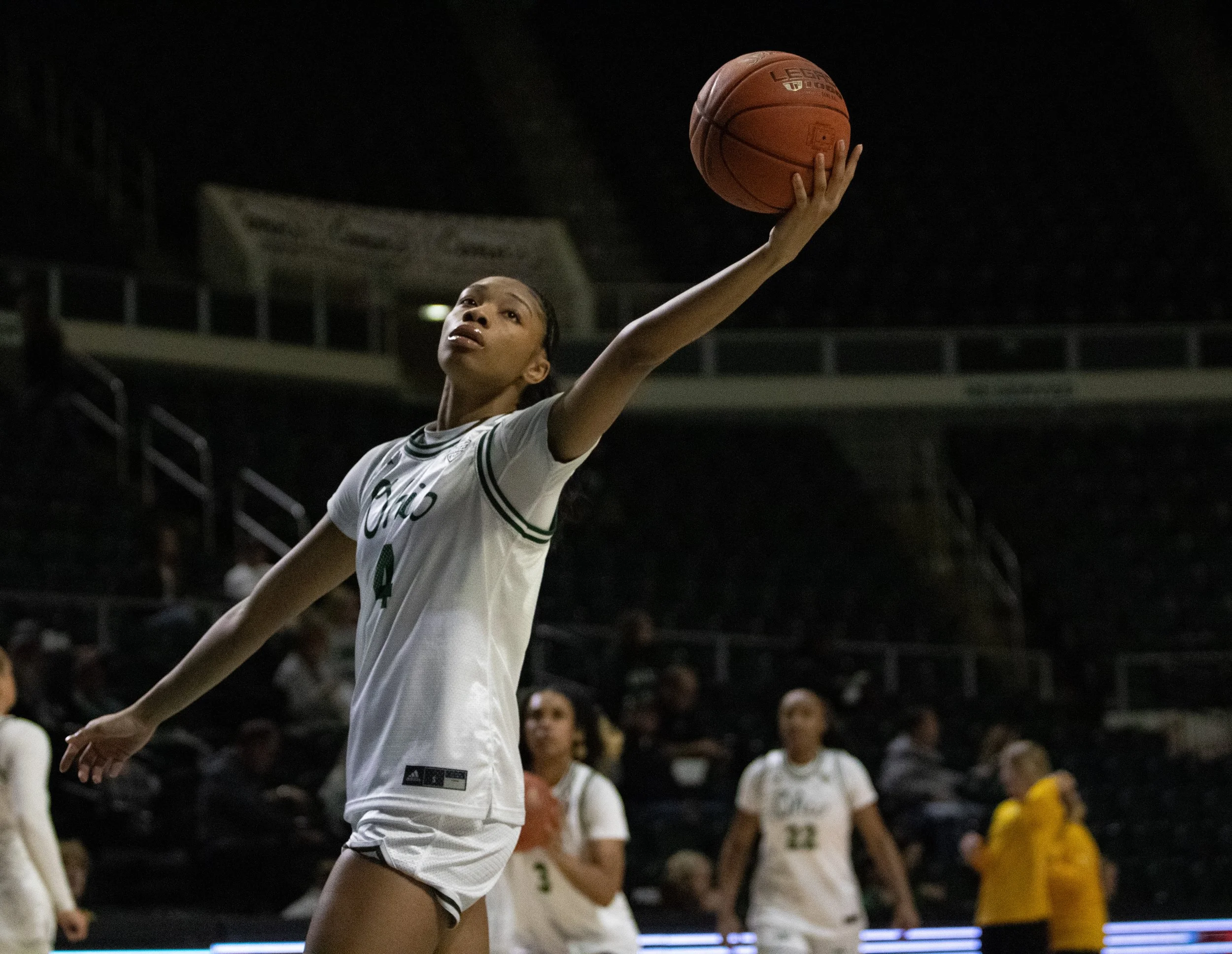 A female basketball player wearing a white uniform with the number 4 on it, jumping to make a shot with her arm extended and holding a basketball, in an indoor arena during a game.