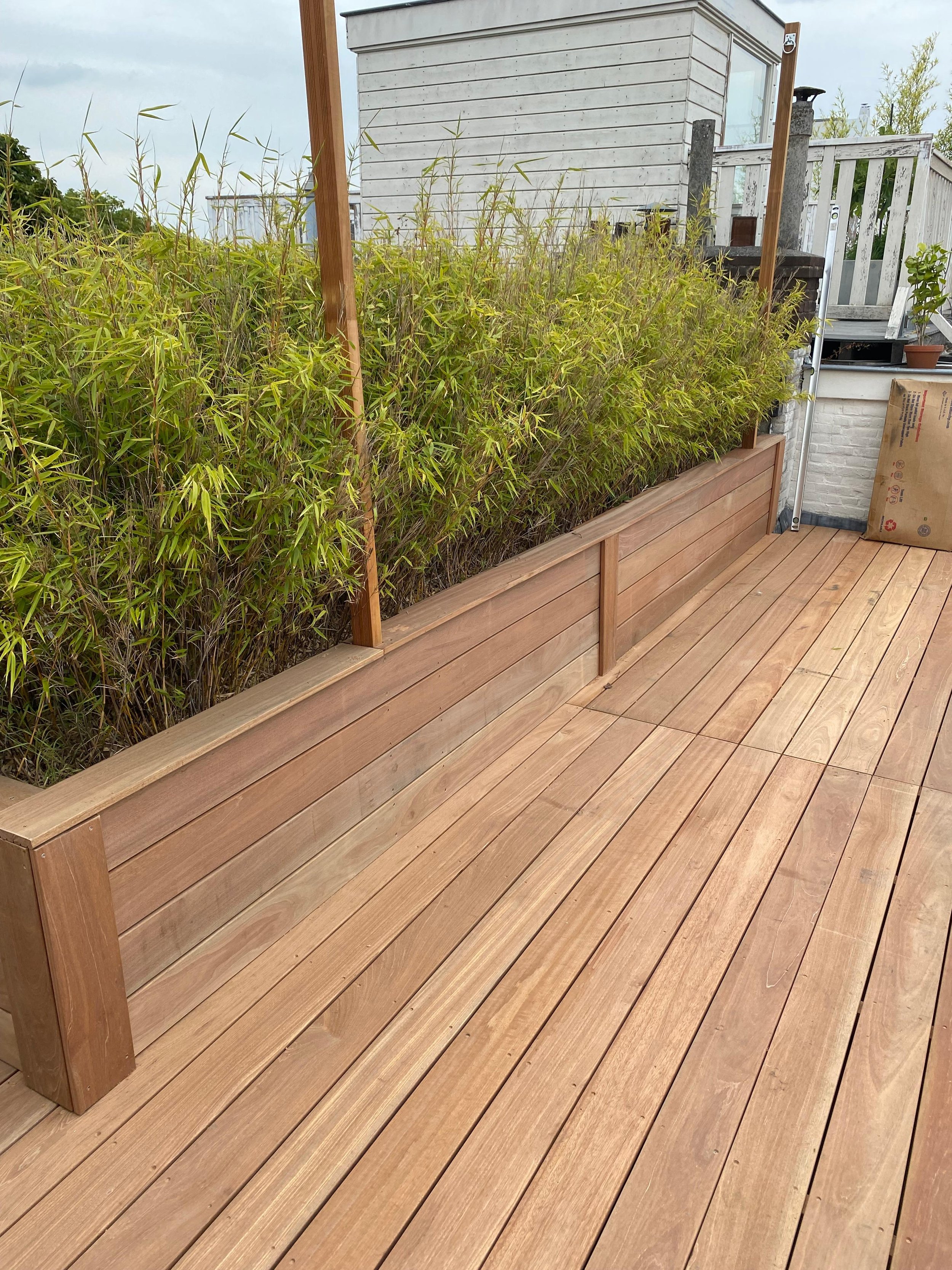 Lange houten bloembak met groene planten en een houten terras.
