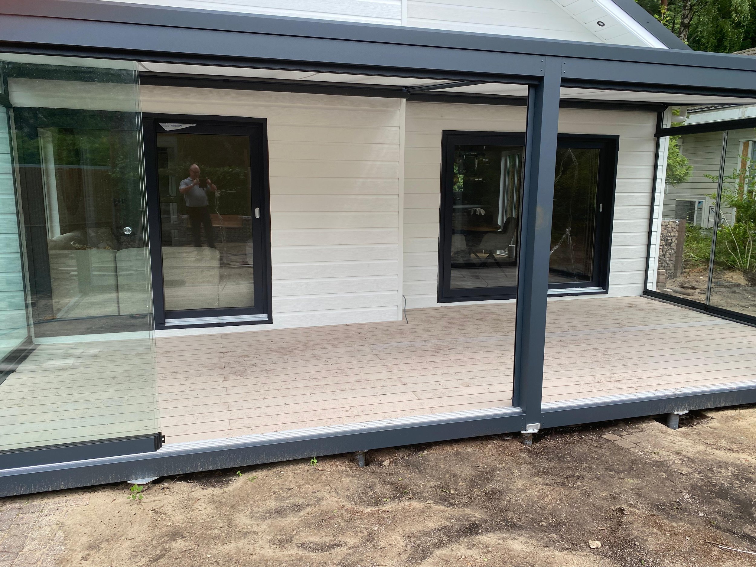 Nieuwe woning met een Composiet terras en zwarte raamkozijnen, gedeeltelijk omgeven door glazen windschermen.