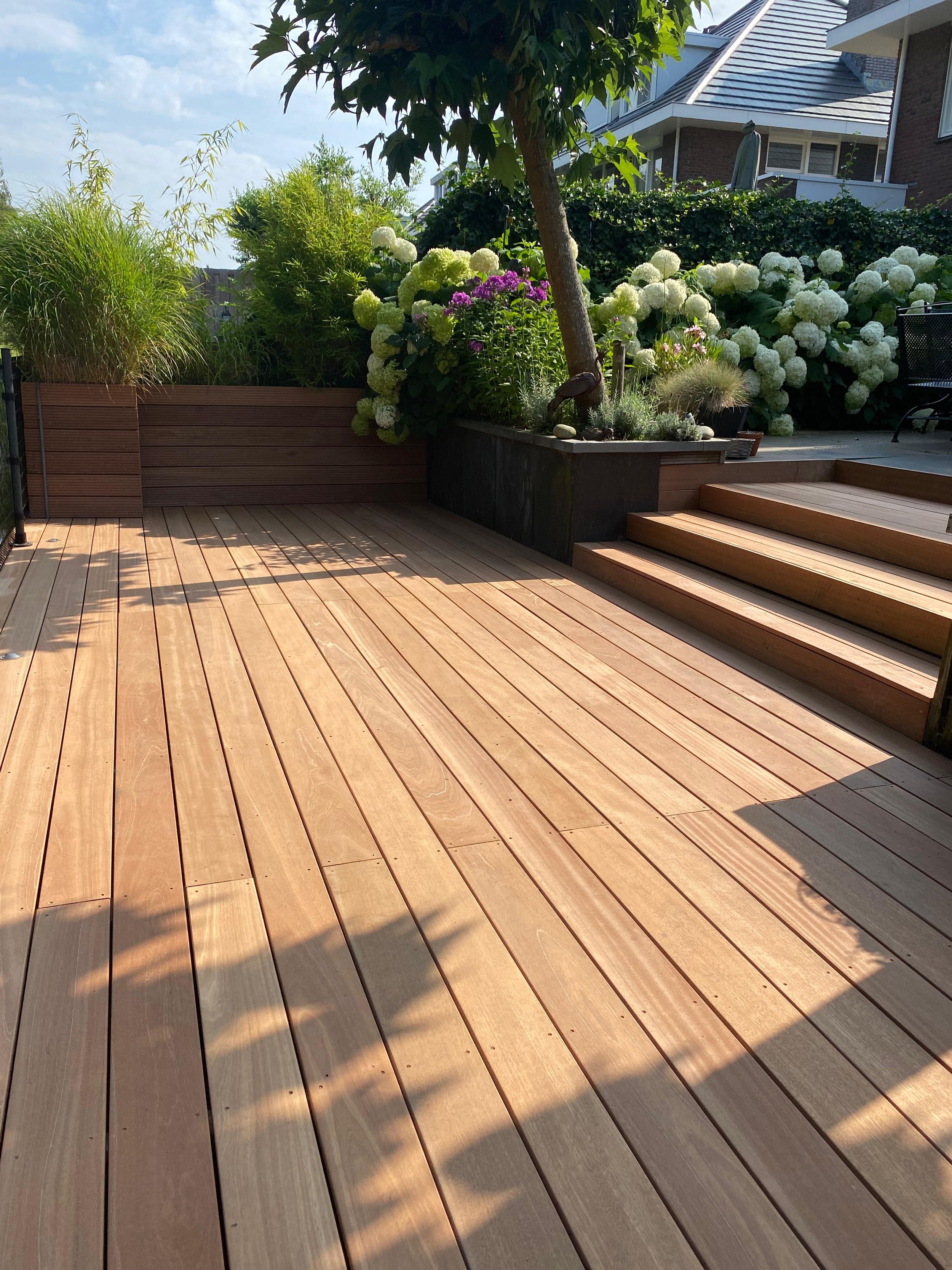 Nieuw aangelegde houten terras met trap, groene planten, bloemen en een boom, buitenruimte in een tuin.