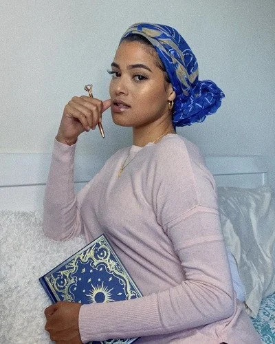 Khristie, the owner of Kumo Studios, in a headscarf and longsleeve sweater with a notebook and pen in hand