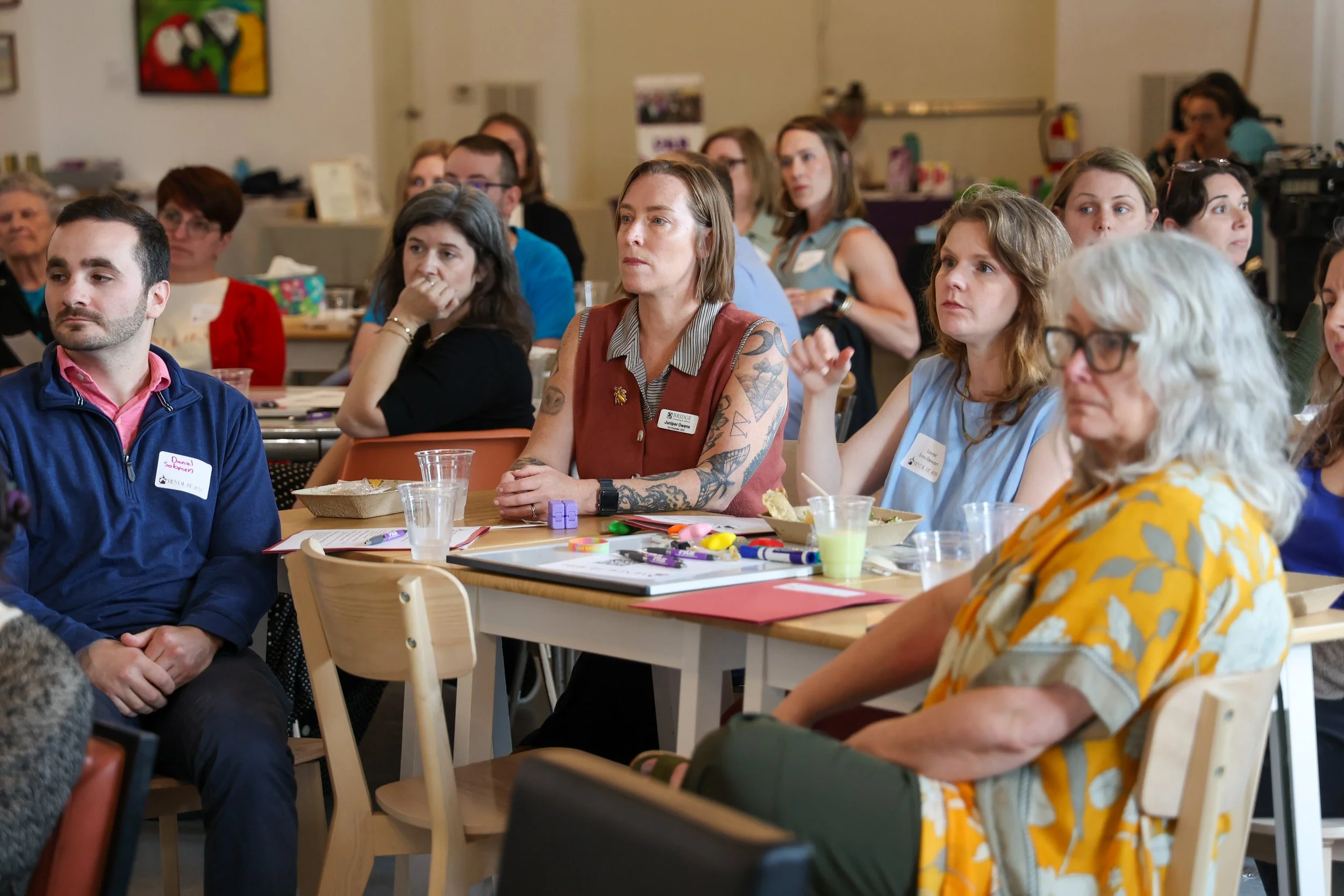 A diverse group of people seated at tables, attentively listening at a conference or workshop.