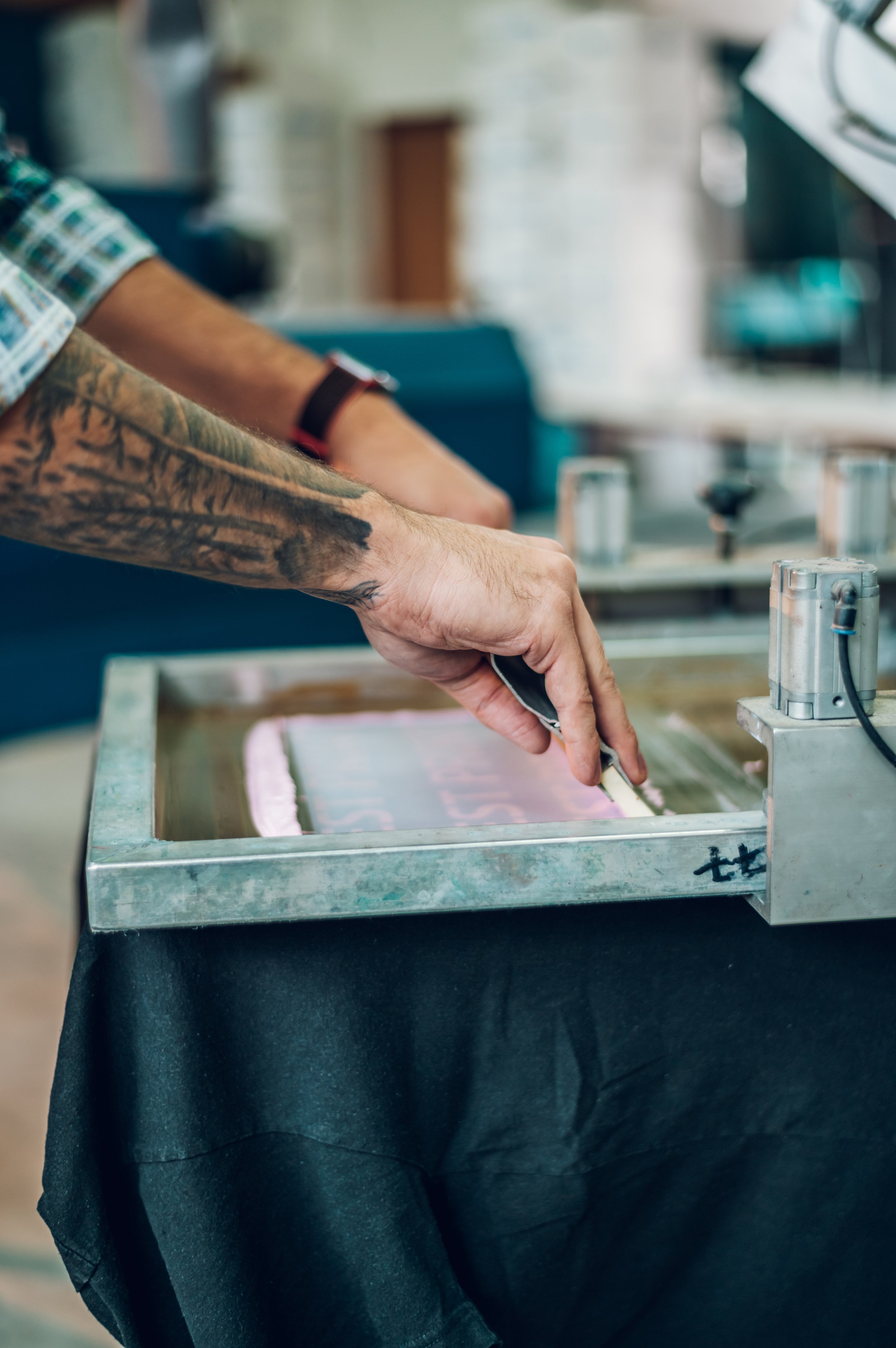 Person screen printing with squeegee; tattooed arm visible.