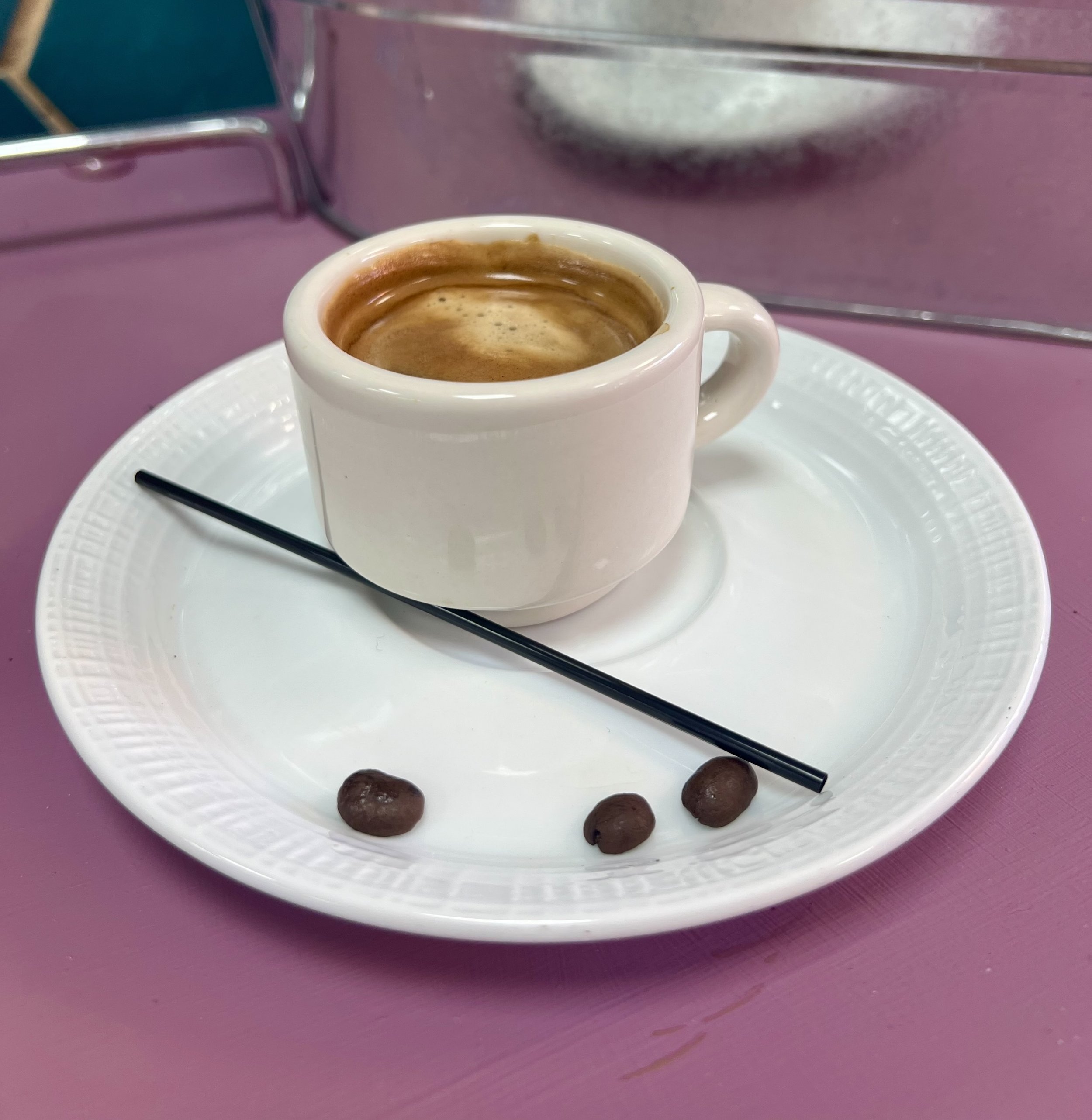 Espresso in white cup with coffee beans and stirrer on plate