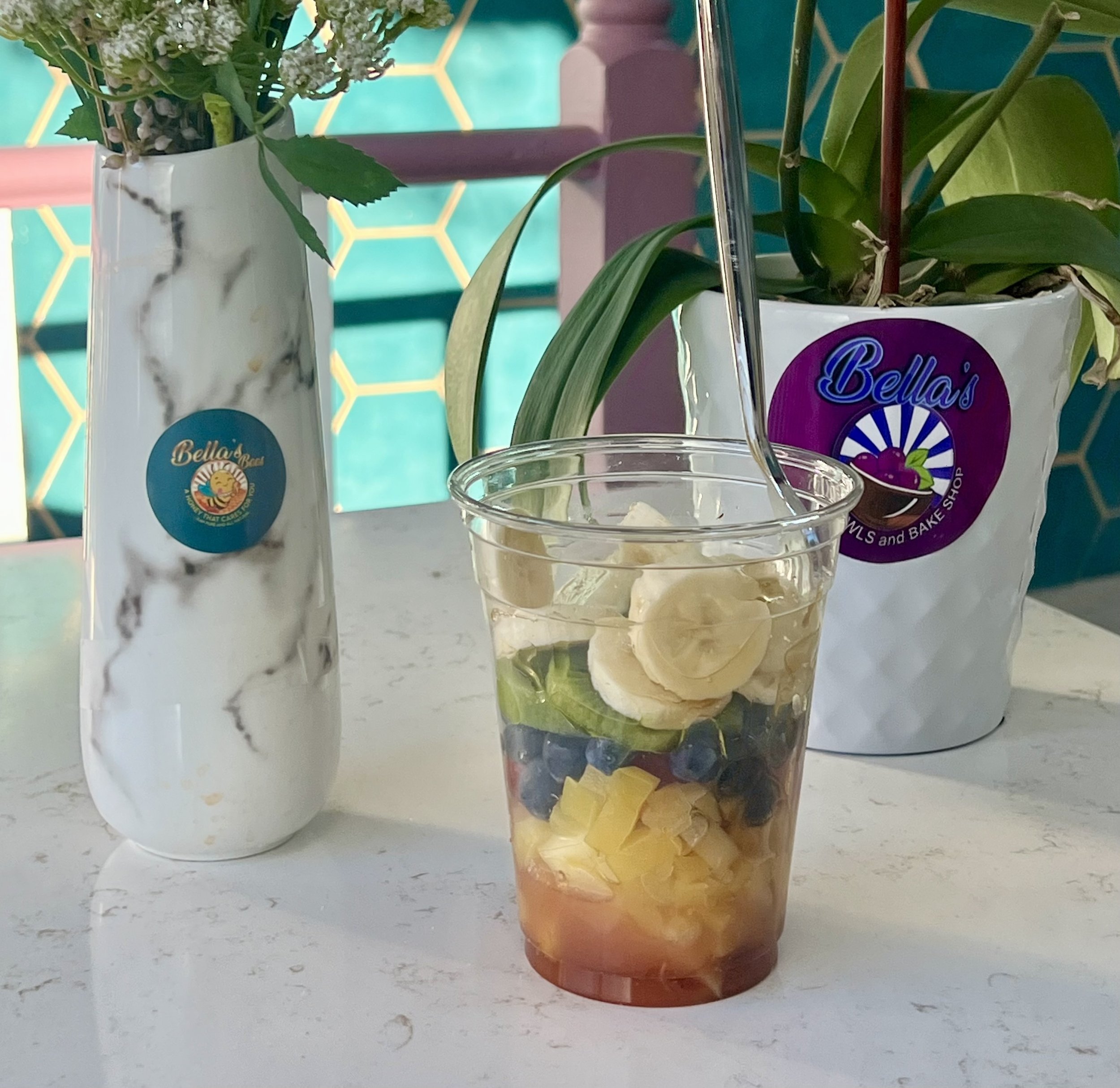 Plastic cup with layered fruit and spoon, next to decorative vases on a marble-style table.