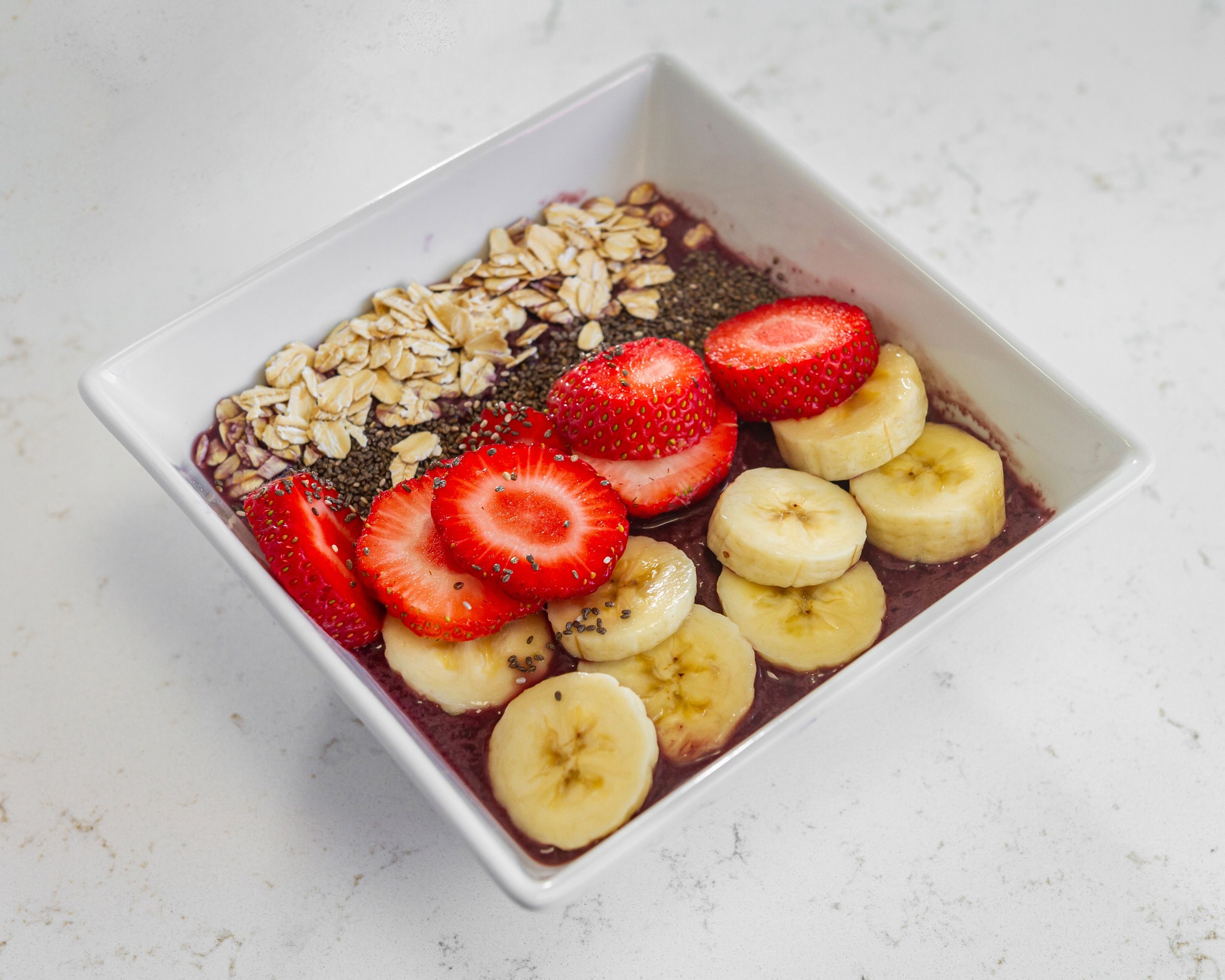 Acai bowl with banana, strawberries, oats, and chia seeds in a white bowl.