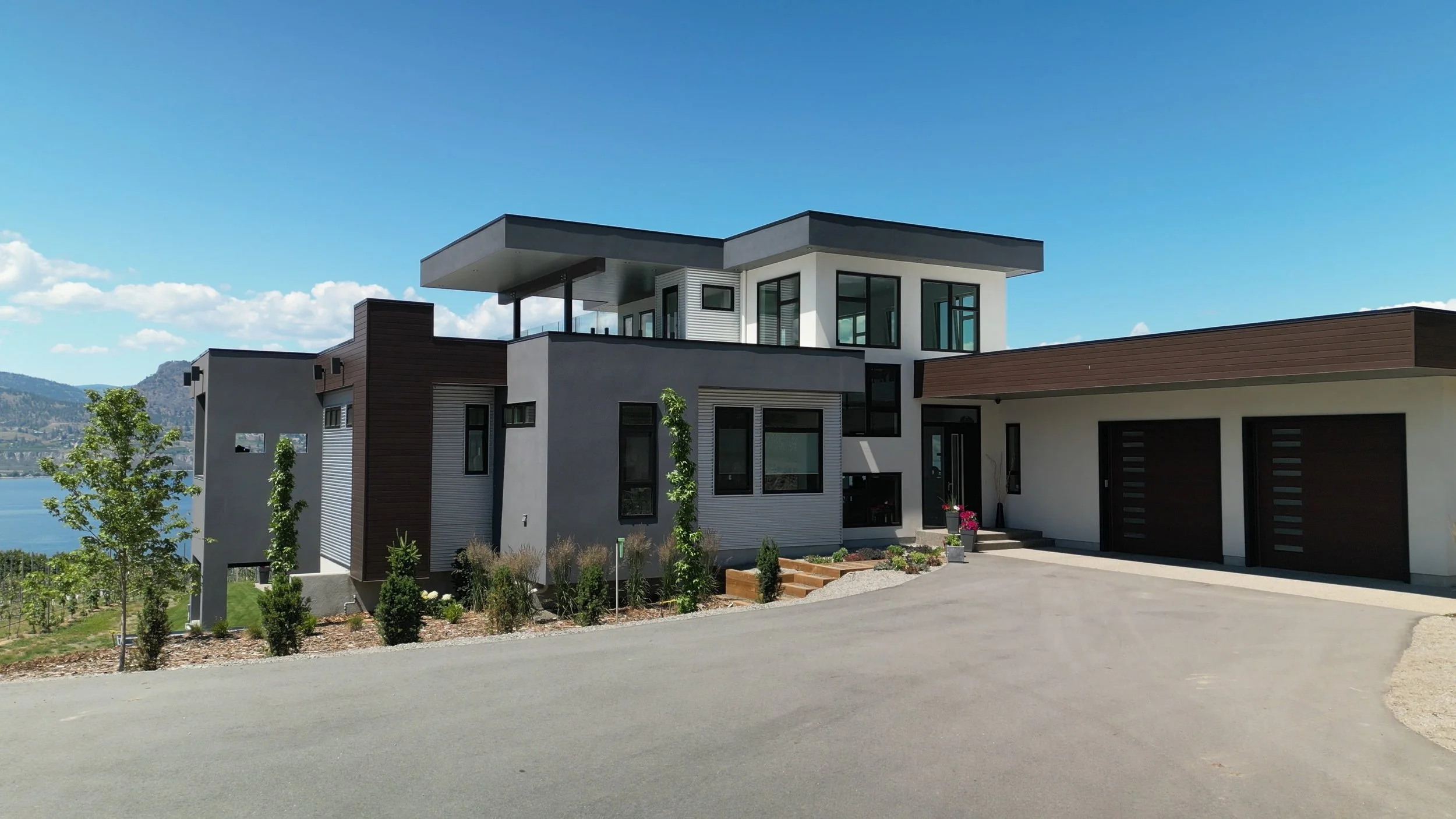 Modern house with large windows, flat roof, and attached garage, located near a Okanagan Lake with scenic views.