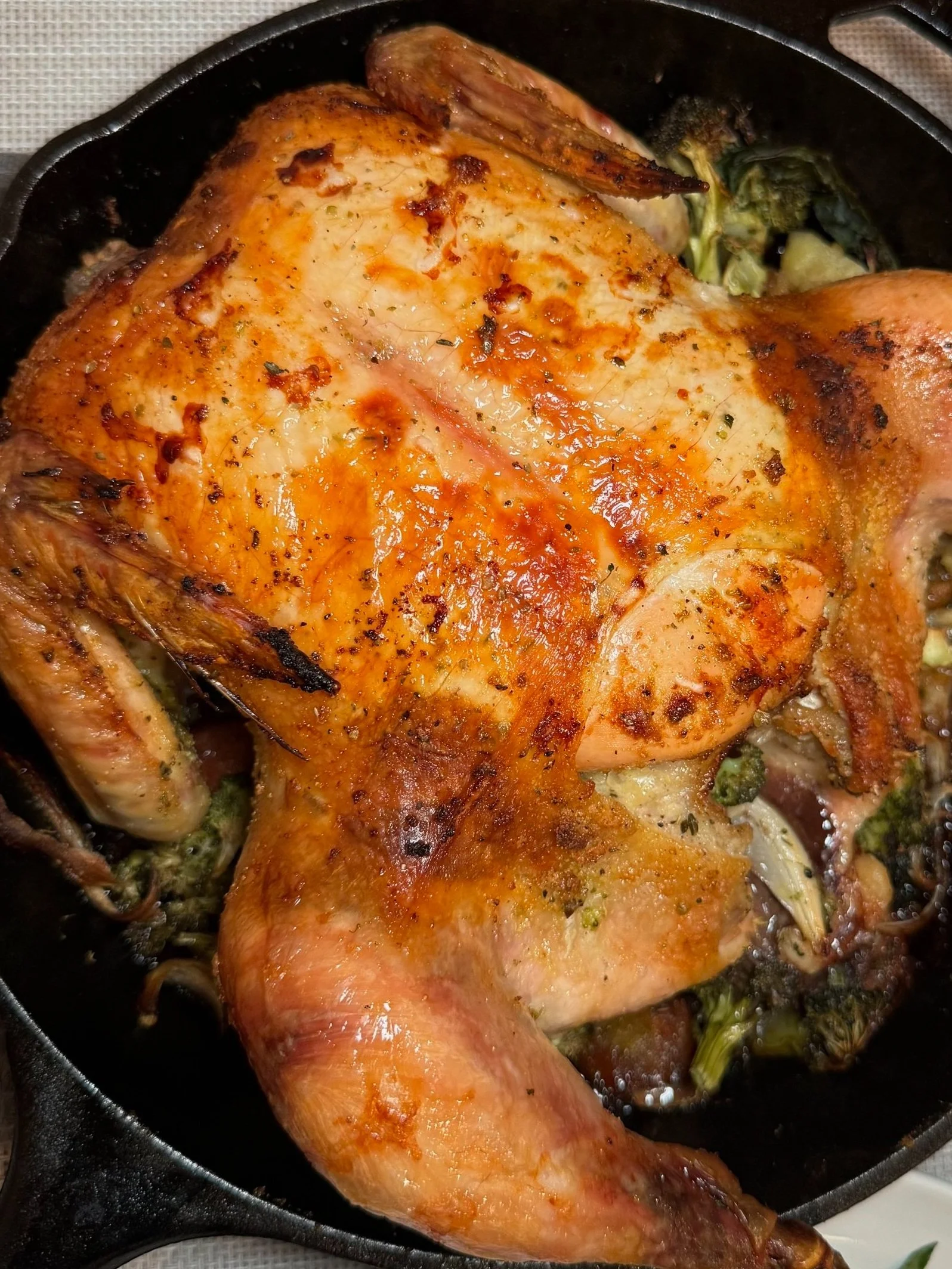 Golden brown roasted whole chicken in a black skillet, with roasted vegetables underneath.
