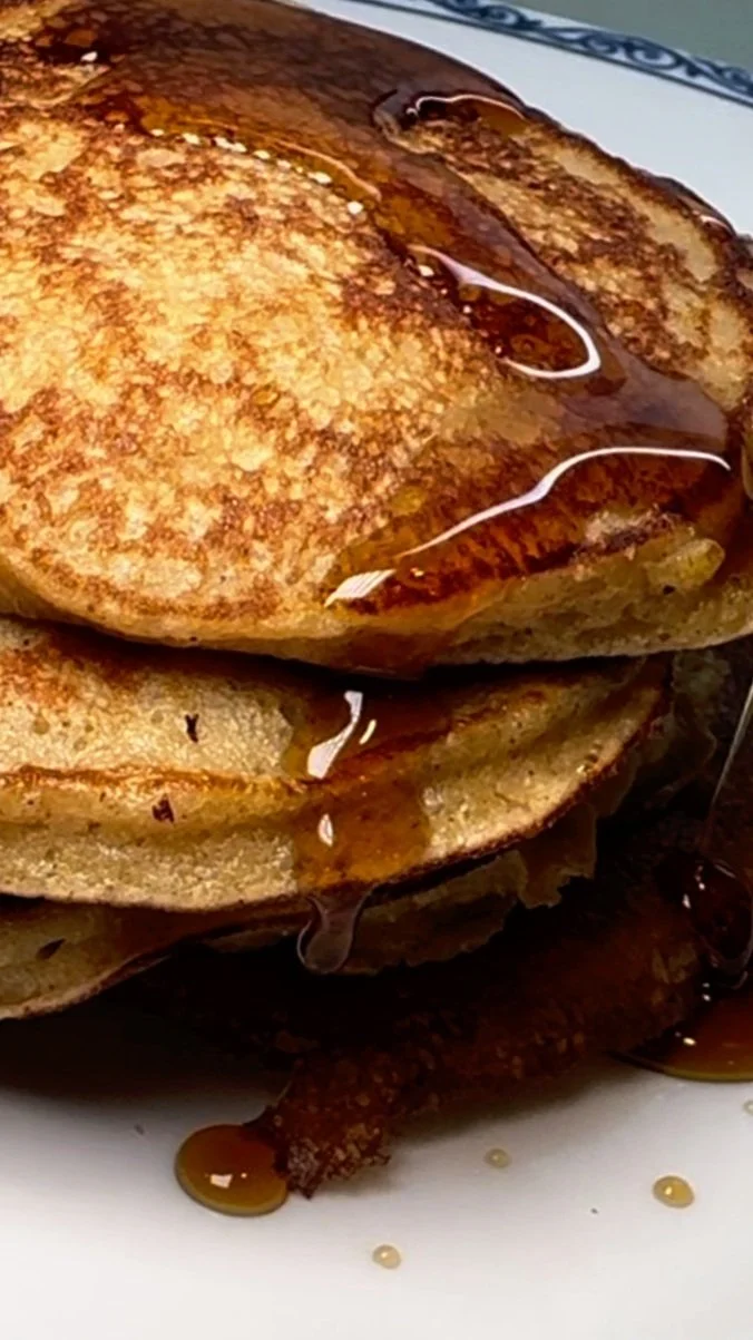 Stack of pancakes drizzled with syrup on a white plate.