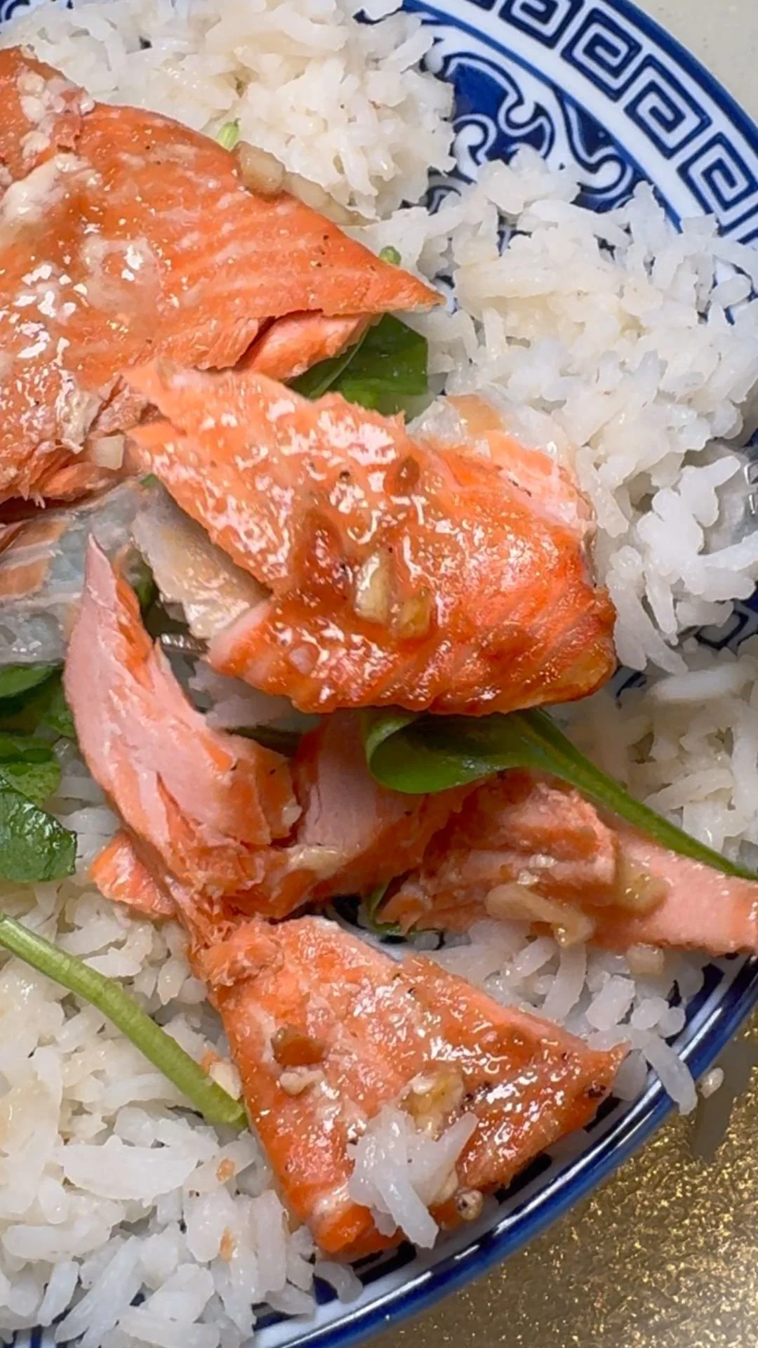 Cooked salmon on a bed of white rice with green herbs and sauce.