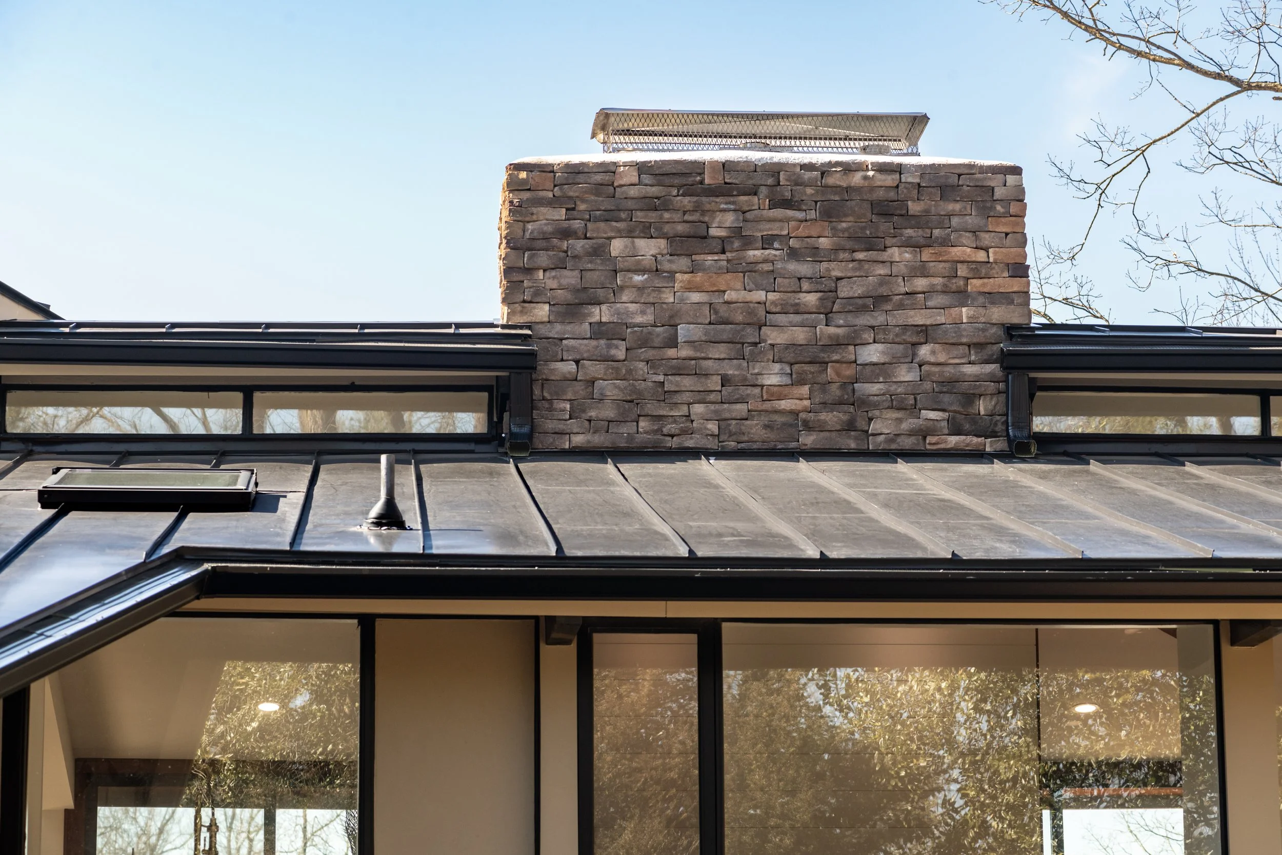 Stone chimney on a modern building with large windows and metal roof.