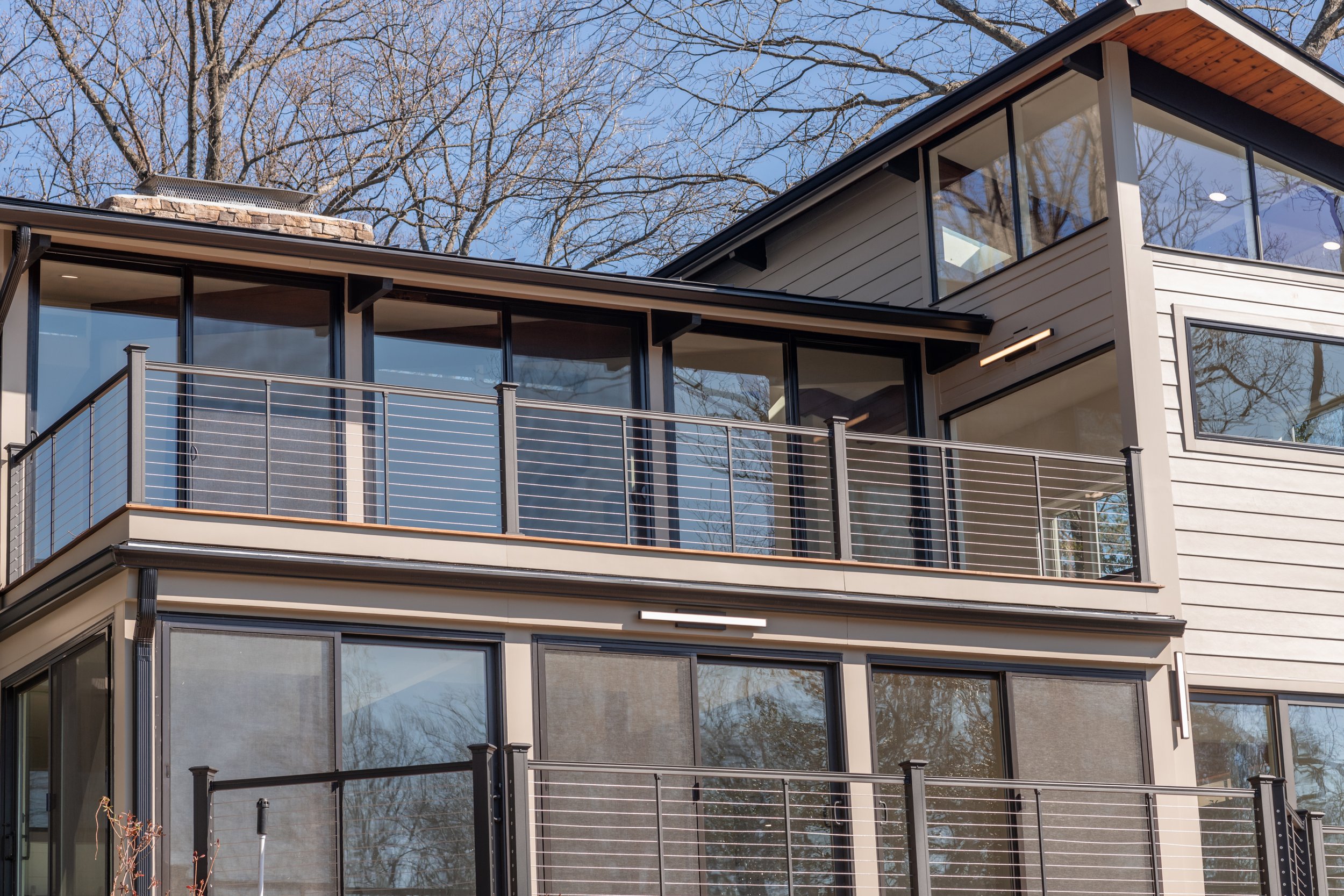 Modern house exterior with large windows and metal railing balconies, surrounded by leafless trees.