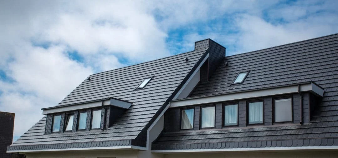 Close-up of a modern house roof with multiple dormer windows and skylights, under a partly cloudy sky.