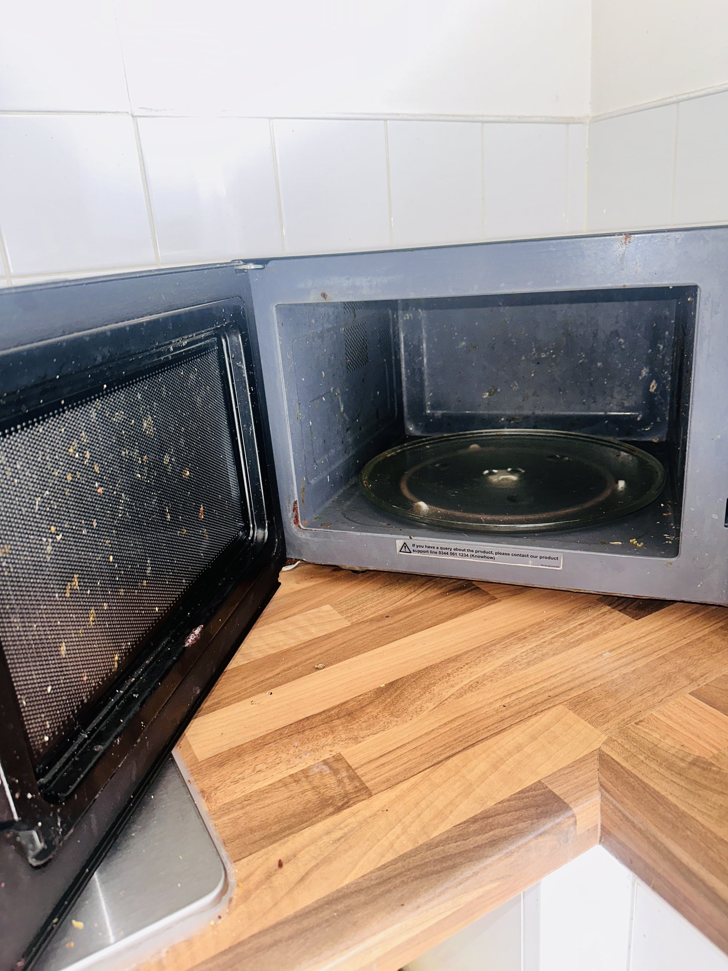 Open microwave with a dirty interior on a wooden countertop.