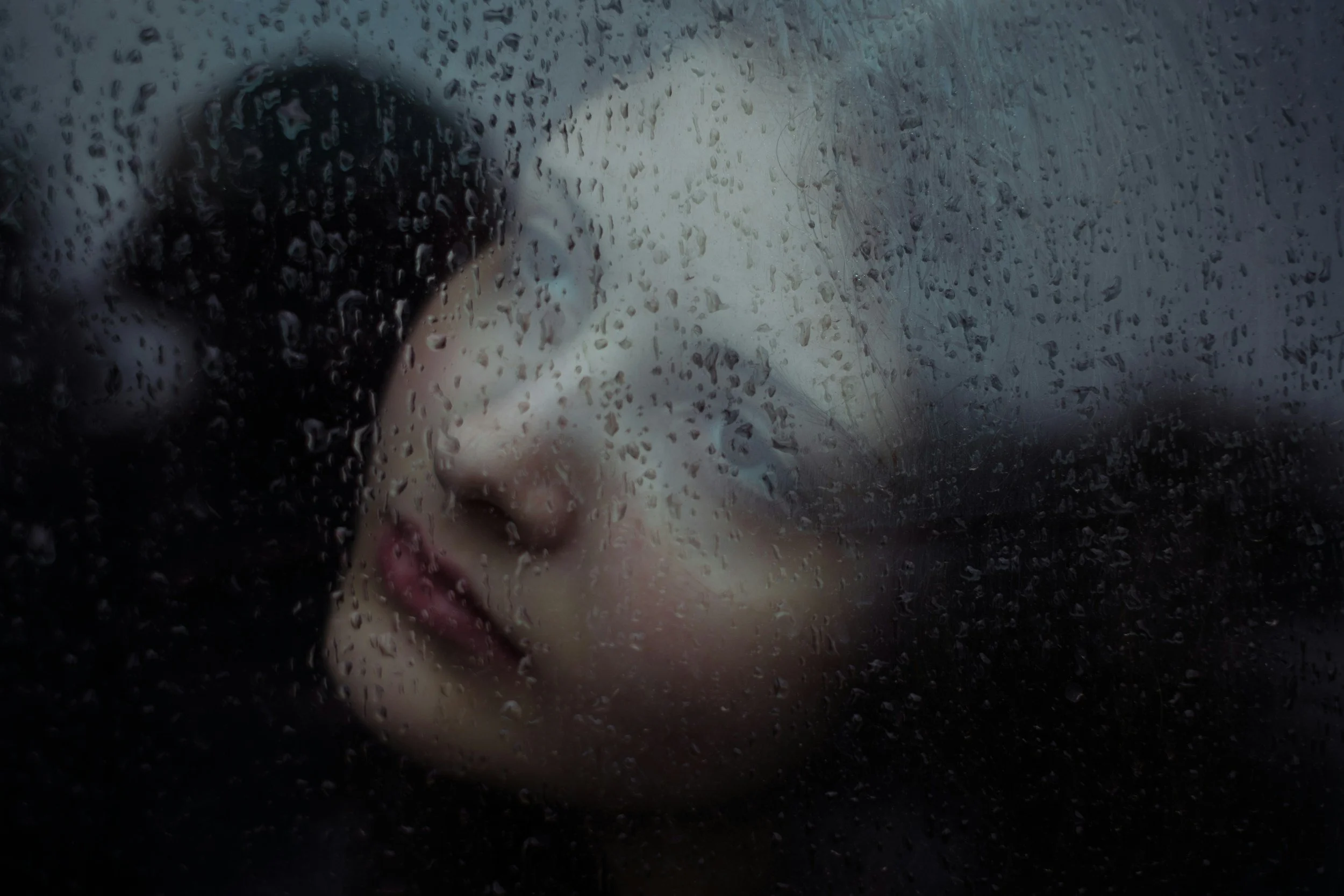 A woman's face with closed eyes seen through a rain-covered glass window, wondering if she needs therapy in Los Feliz