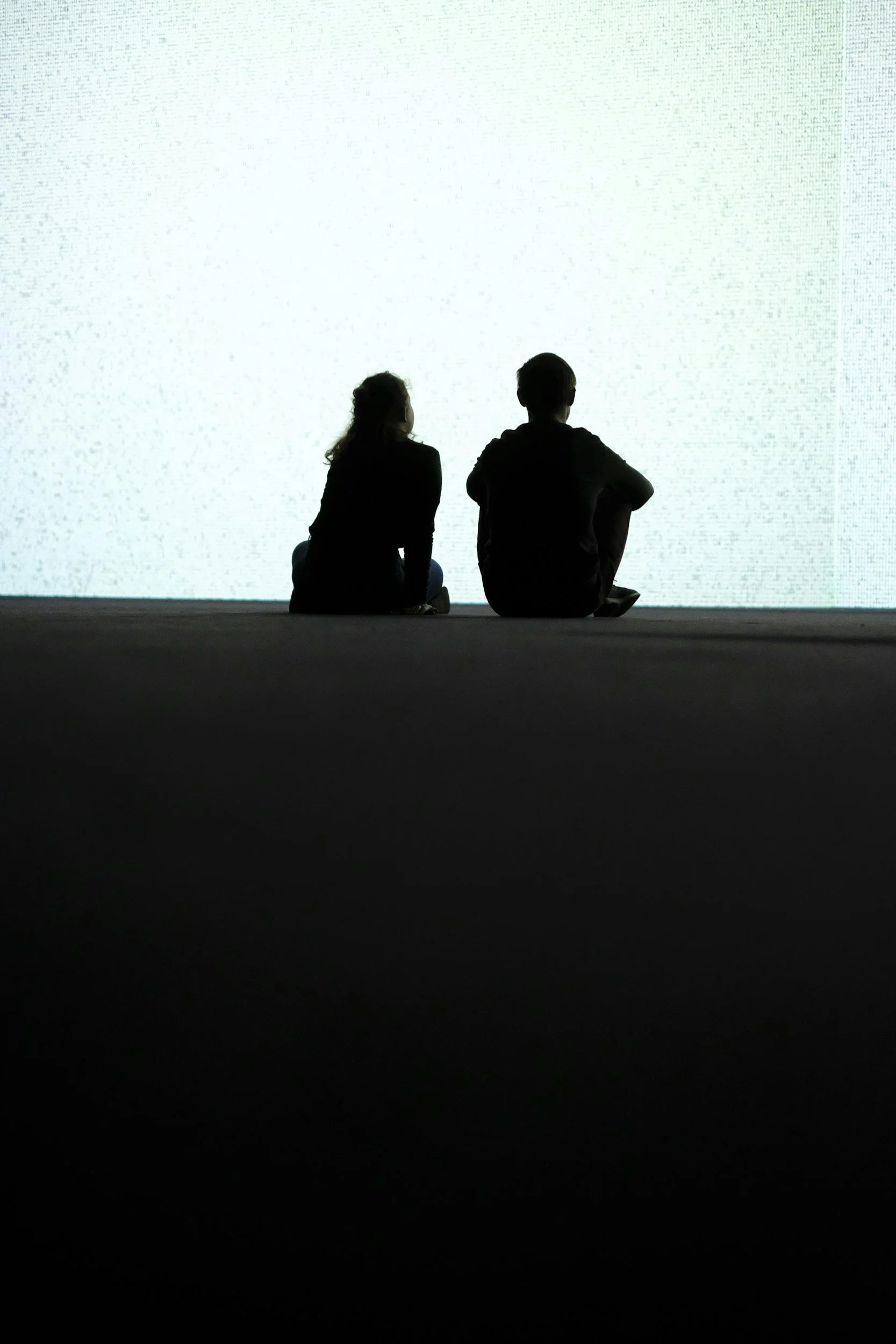 A silhouetted couple sitting on the floor facing a bright white wall or screen, contemplating couples therapy in Los Angeles.