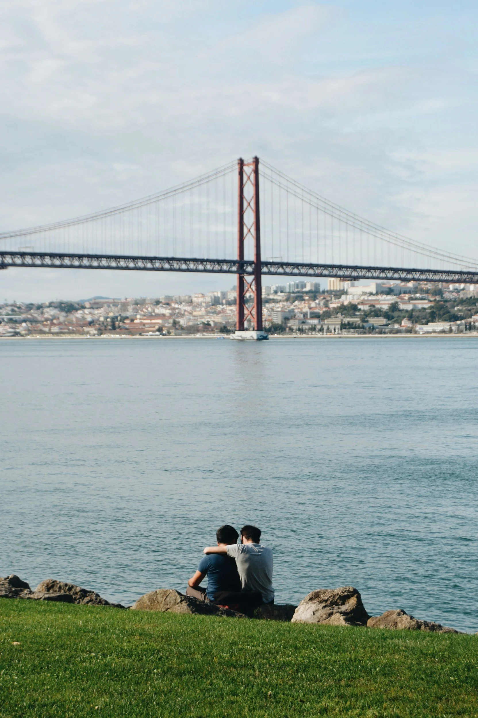 A couple sitting on rocks by the water, with a bridge and city skyline in the background, connected after attending couples therapy in Los Angeles.