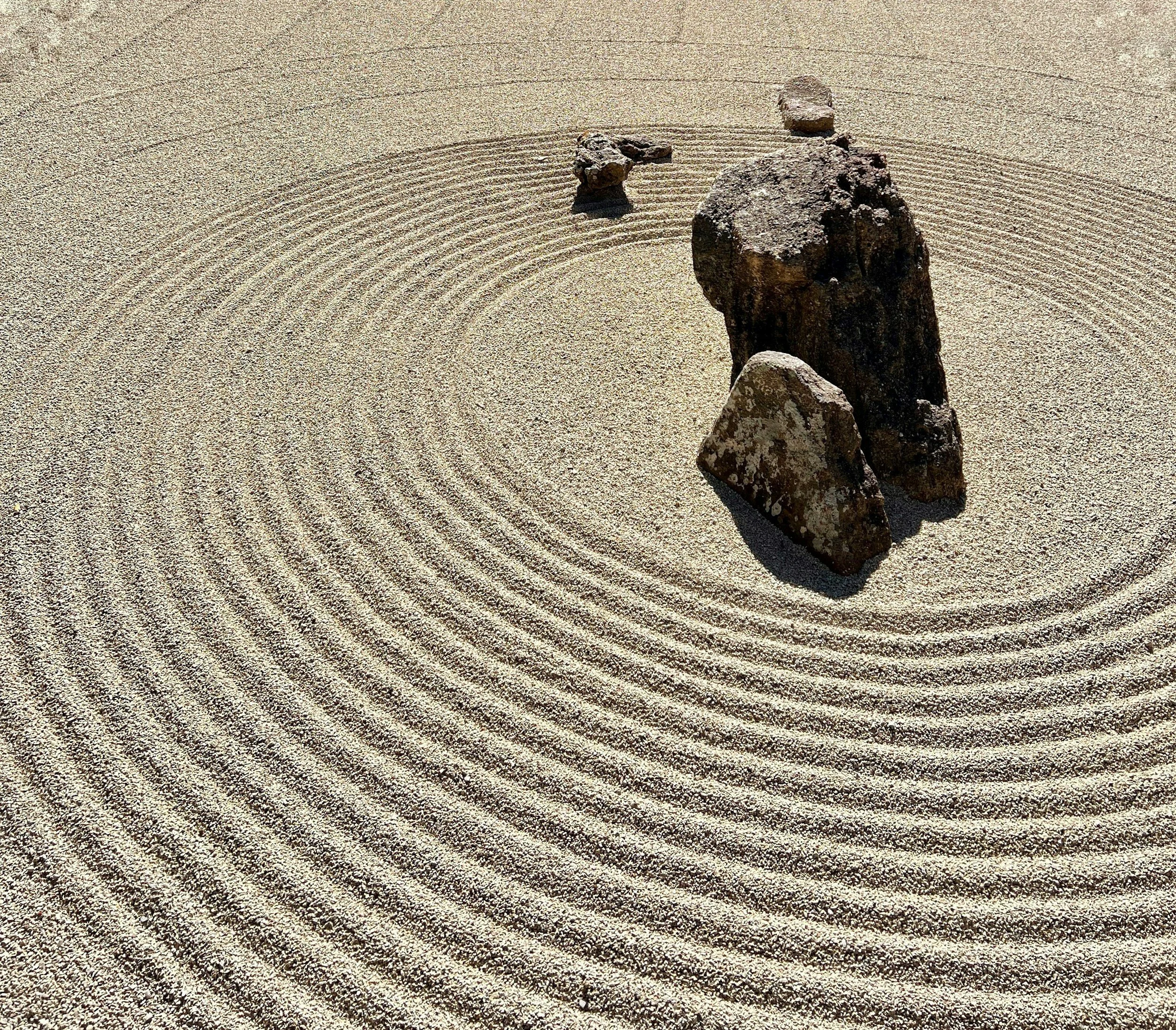 Concentric circles drawn in sand with large rocks in the middle representing the patterns that emerge in therapy.
