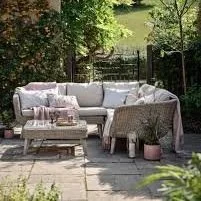 Outdoor patio with a large L-shaped sofa, pillows, and blankets, surrounded by trees.