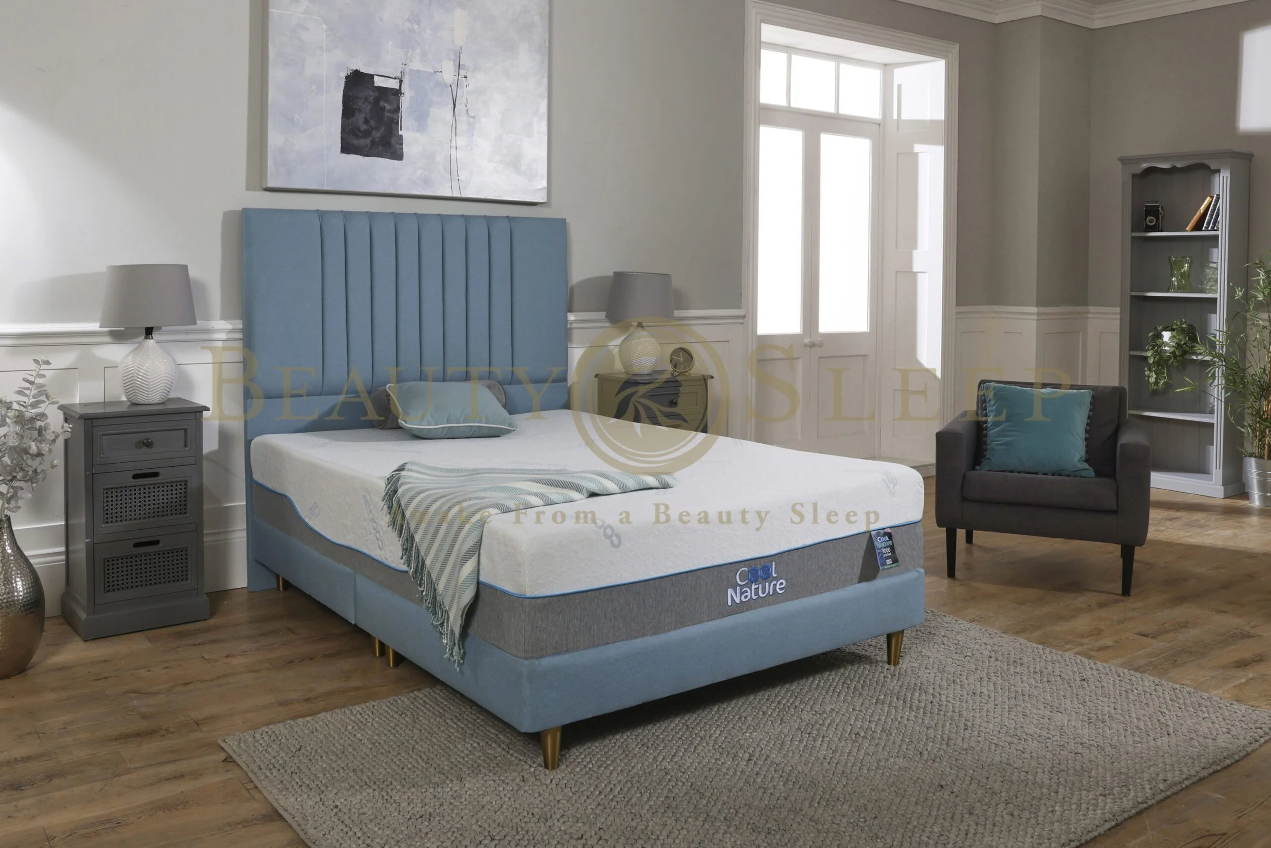 A bedroom with a blue upholstered bed with a matching headboard, nightstands on each side, and a water-related themed mattress labeled 'Cool Nature'. There is a gray armchair with a blue pillow, a bookshelf, and a large window in the room.