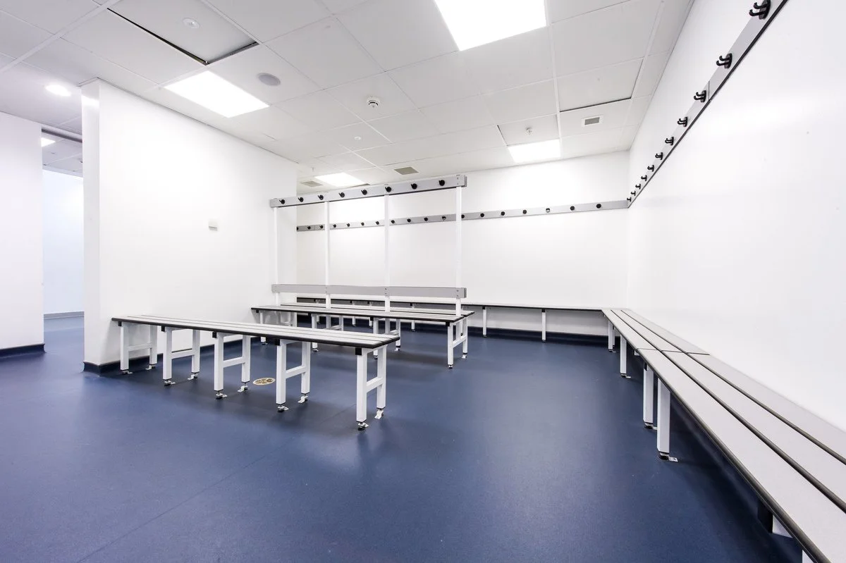 Direct flooring suppliers of driffield, commercial flooring, Empty locker room with white benches, white walls, and hooks on the wall.