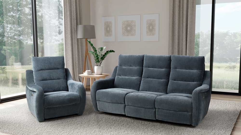 Living room with blue armchair and sofa, side table with plant, large window with curtains, and framed wall art
