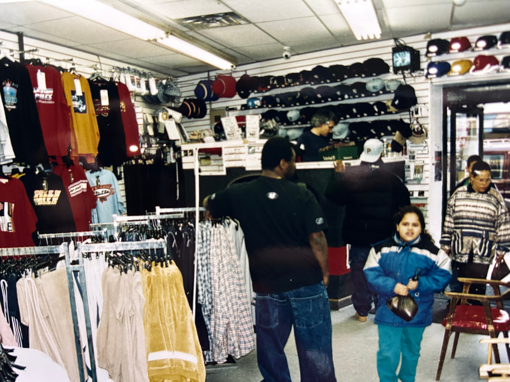 People shopping inside a retail store with clothing, hats, and sports merchandise on display.